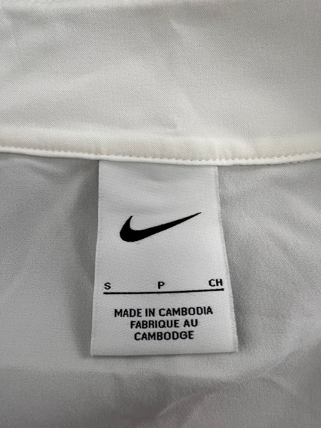 Inside label of cream Nike jacket showing size small and made in Cambodia