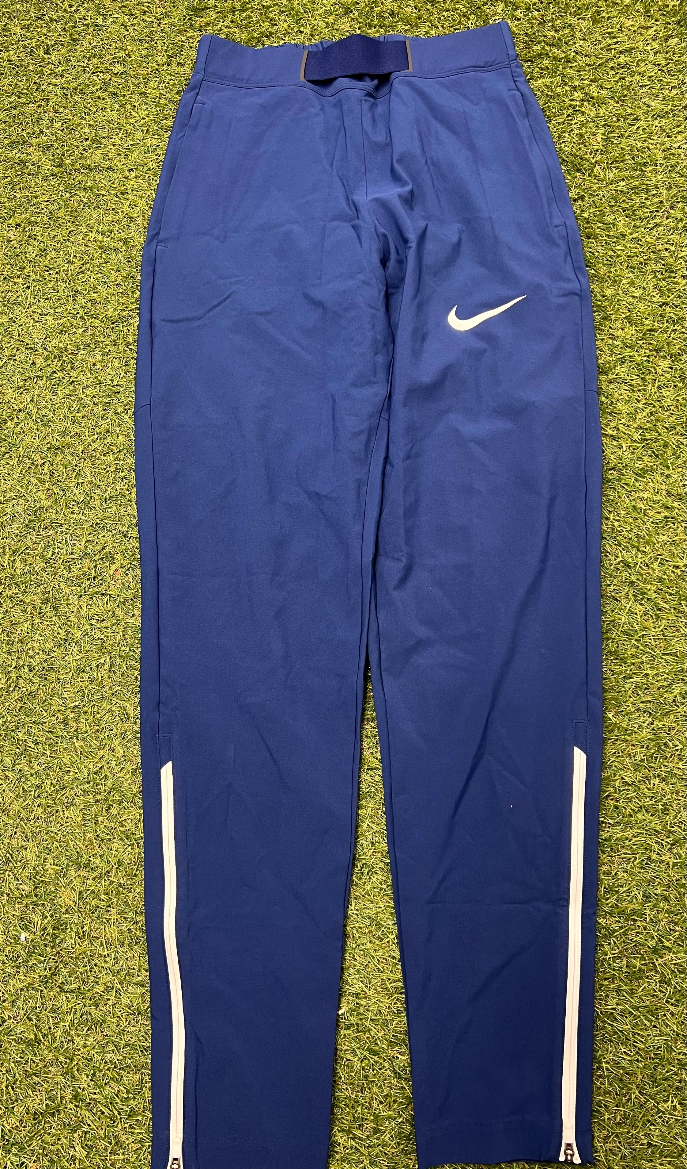 Front view of blue Nike women's training pants with white Nike swoosh and white ankle zippers laid flat on grass