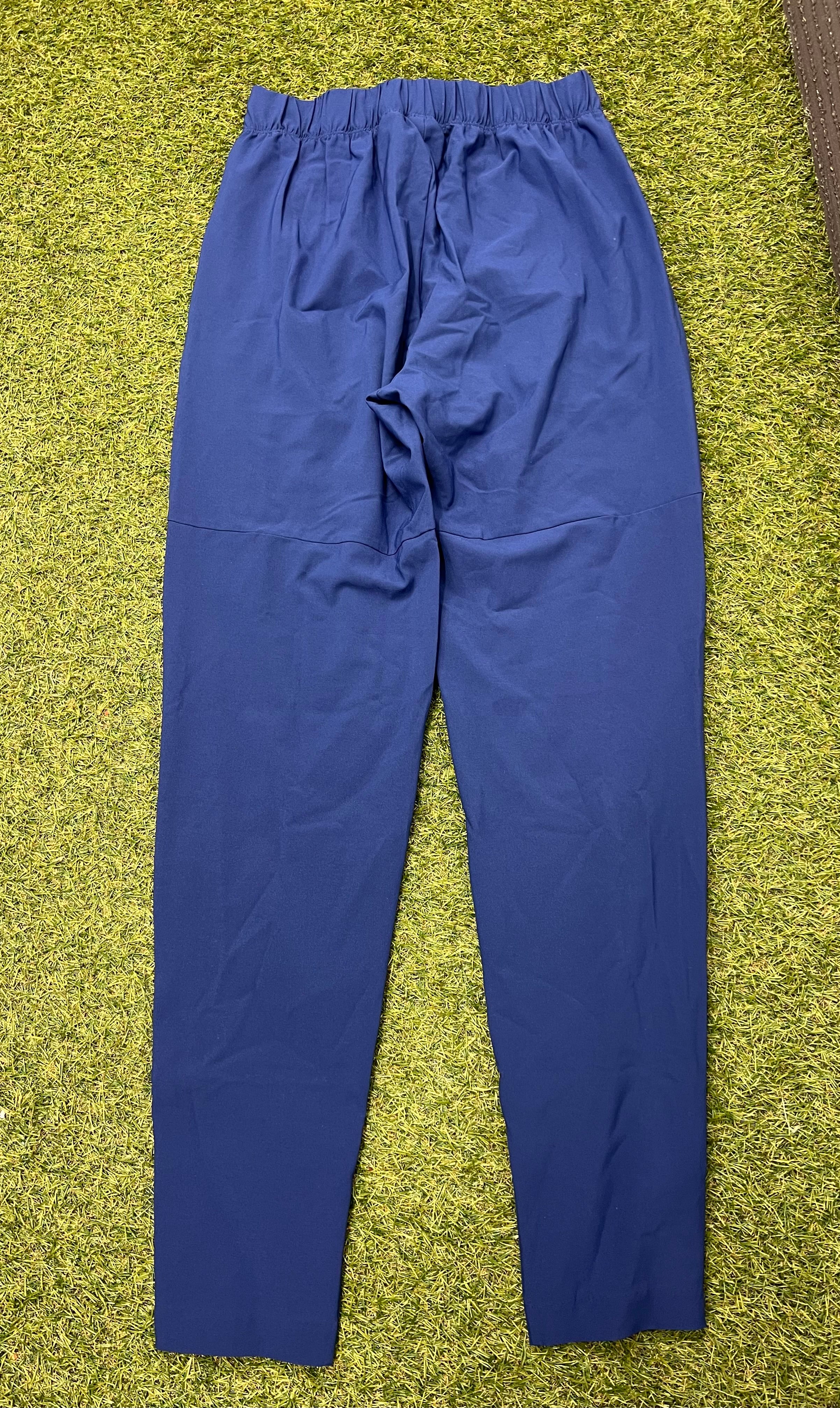 Back view of blue Nike women's training pants showing elastic waistband and plain back laid flat on grass