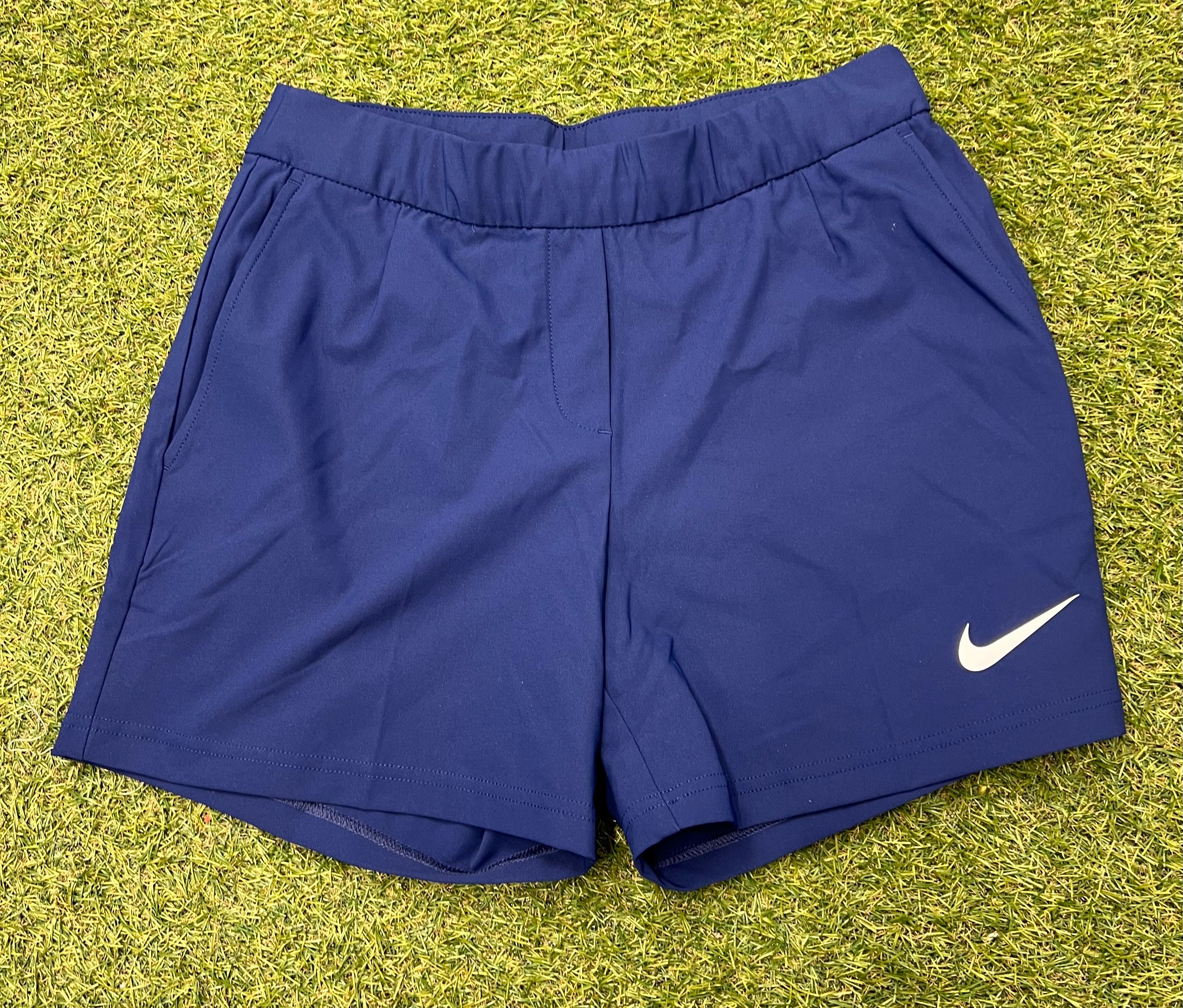 Front view of navy blue Nike women's sports shorts with white Nike logo on the left leg, laid flat on grass