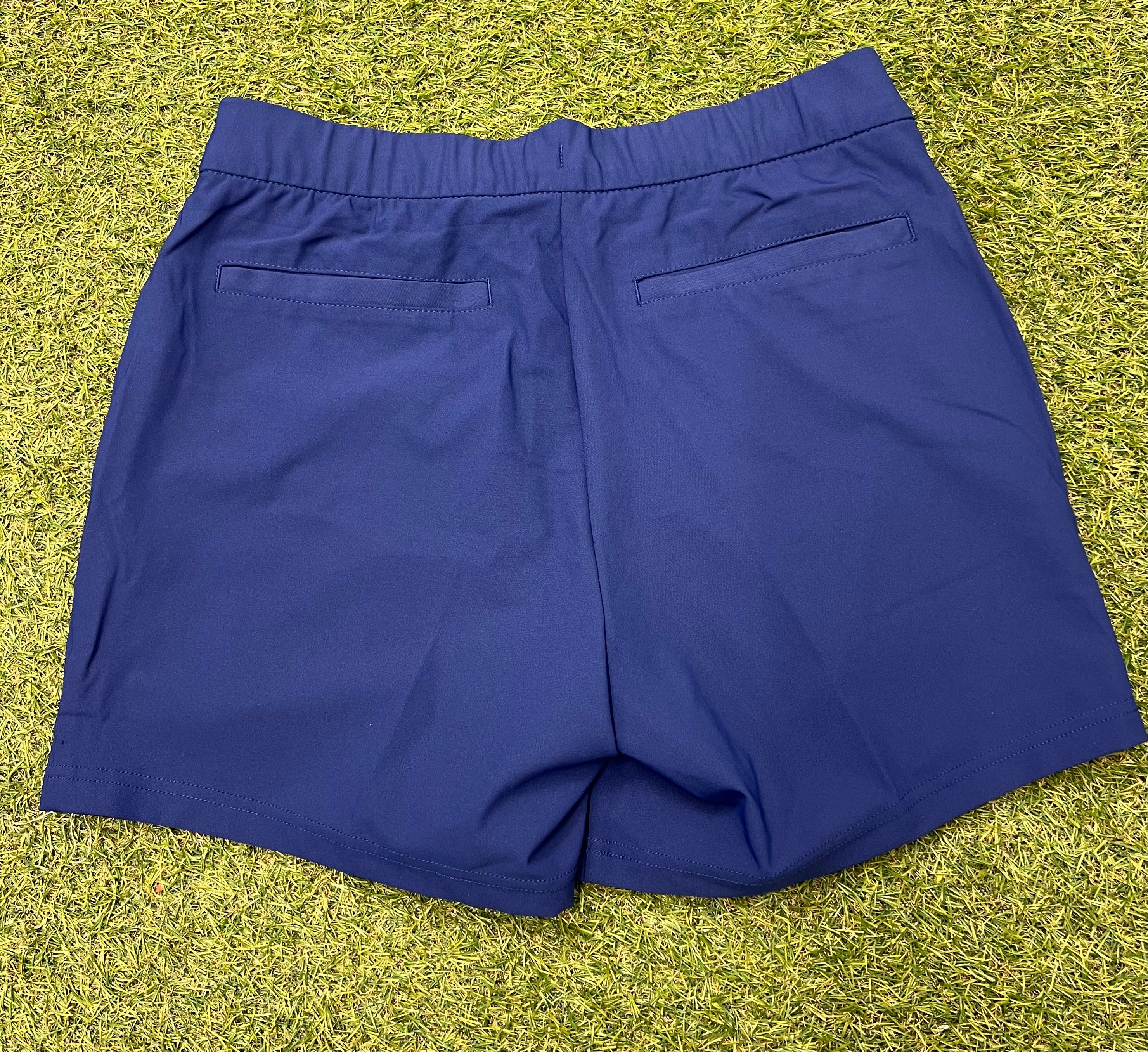 Back view of navy blue Nike women's sports shorts showing elasticated waistband and two back welt pockets on grass