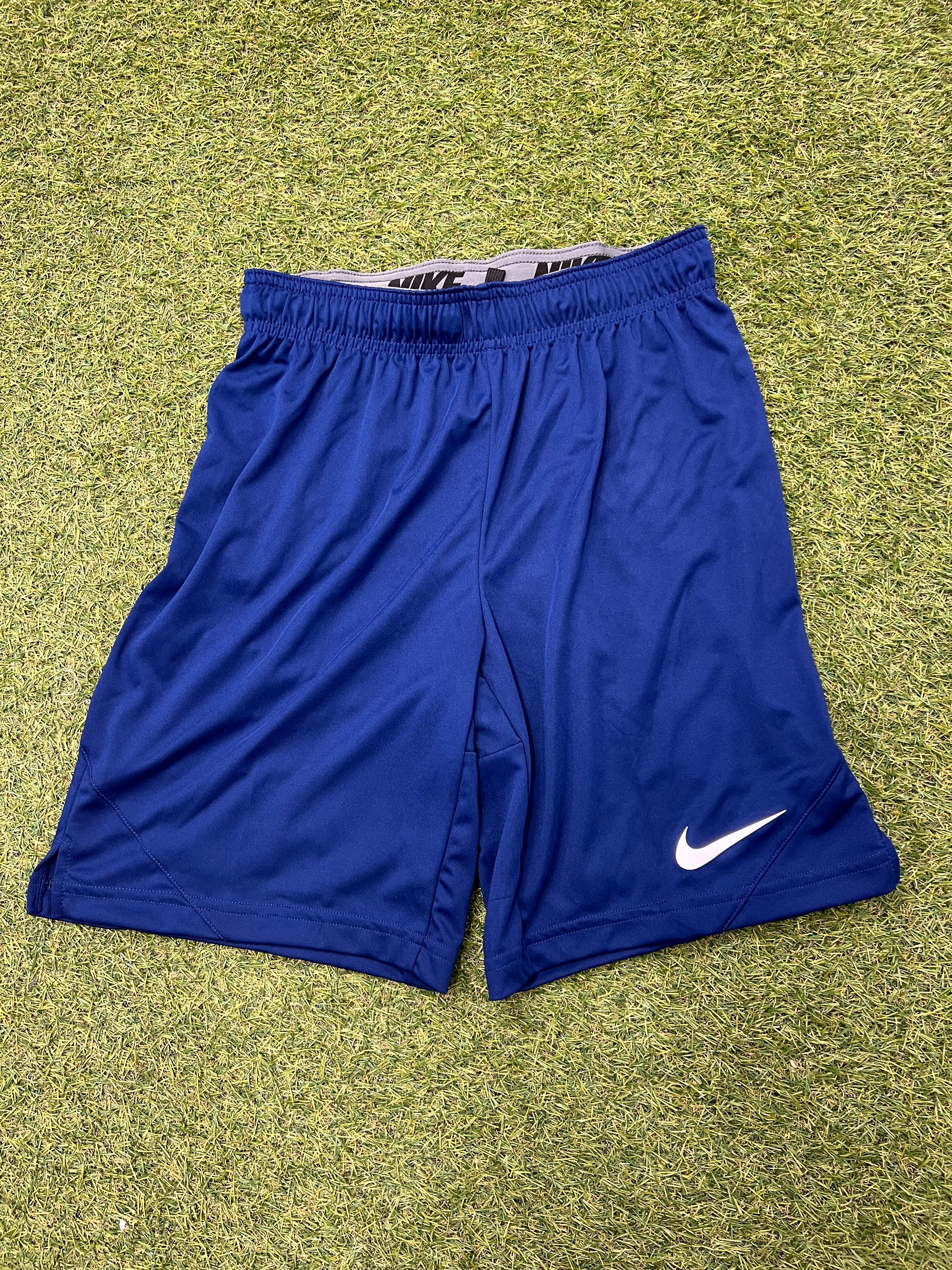 Front view of blue Nike sports shorts on grass showing Nike logo on the left hem