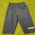 Front view of Kids Kooga Power Rugby Shorts in navy blue laying flat on grass surface