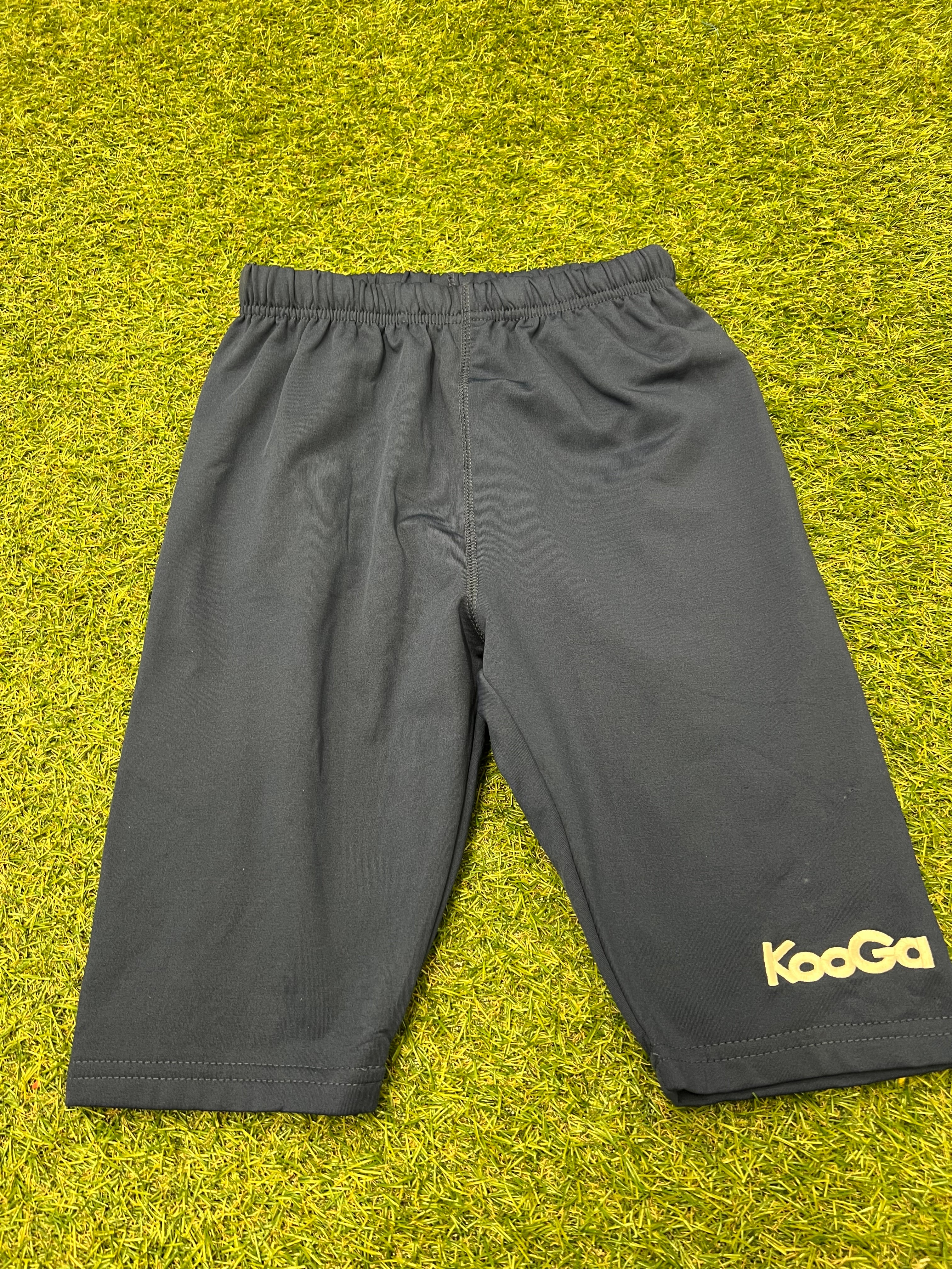 Front view of Kids Kooga Power Rugby Shorts in navy blue laying flat on grass surface