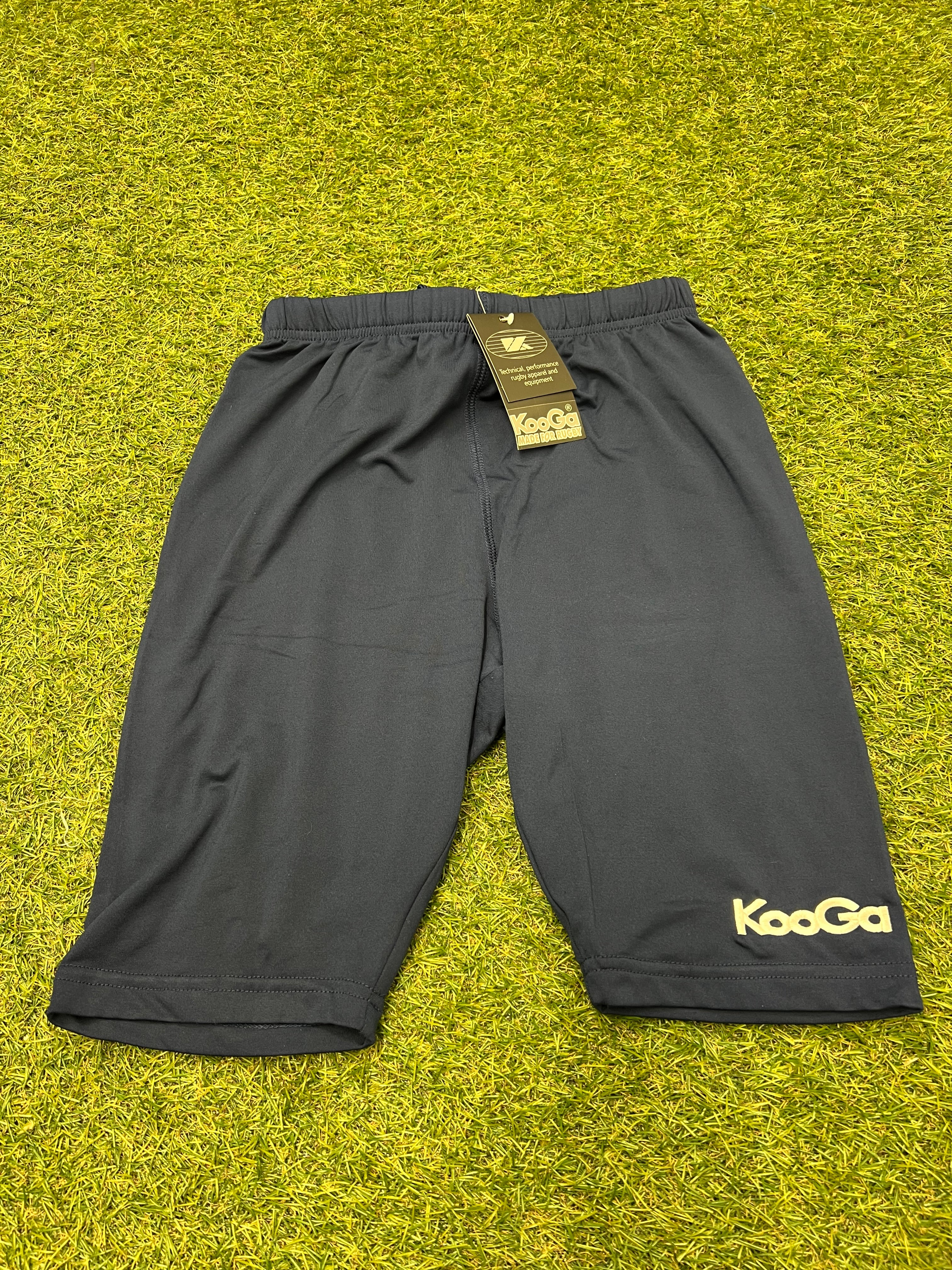Front view of navy KooGa base layer shorts laid flat on grass surface with tag visible
