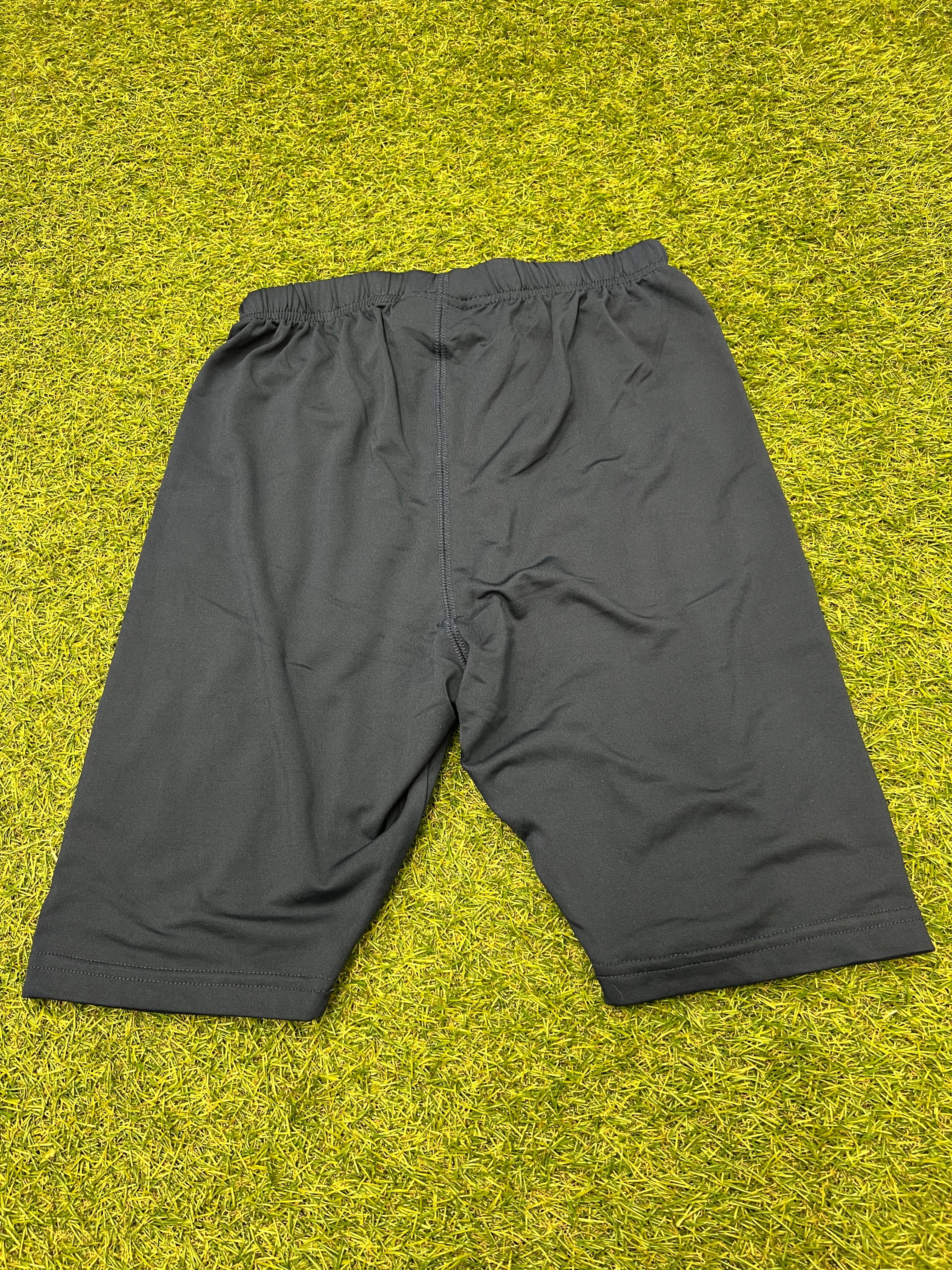 Back view of navy KooGa base layer shorts laid flat on grass surface showing elastic waistband