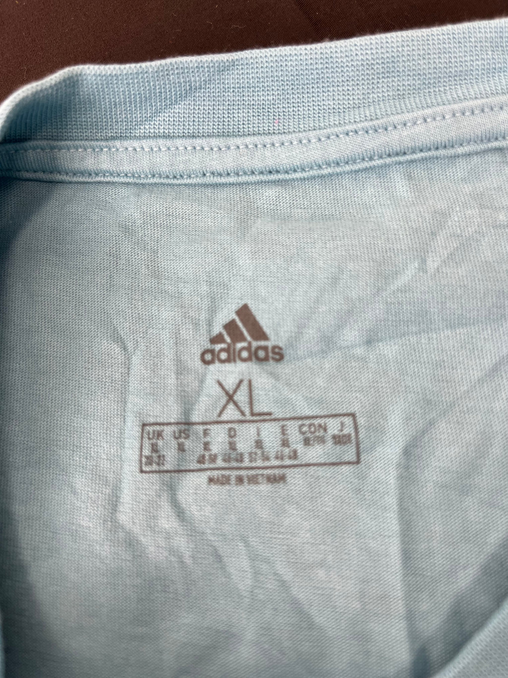 Close-up of the adidas brand label and size XL printed inside the neck of the turquoise t-shirt