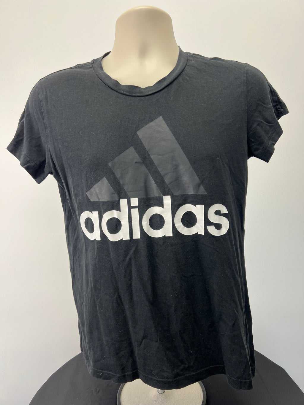 Front view of Adidas women's black t-shirt with large white and dark grey Adidas logo.