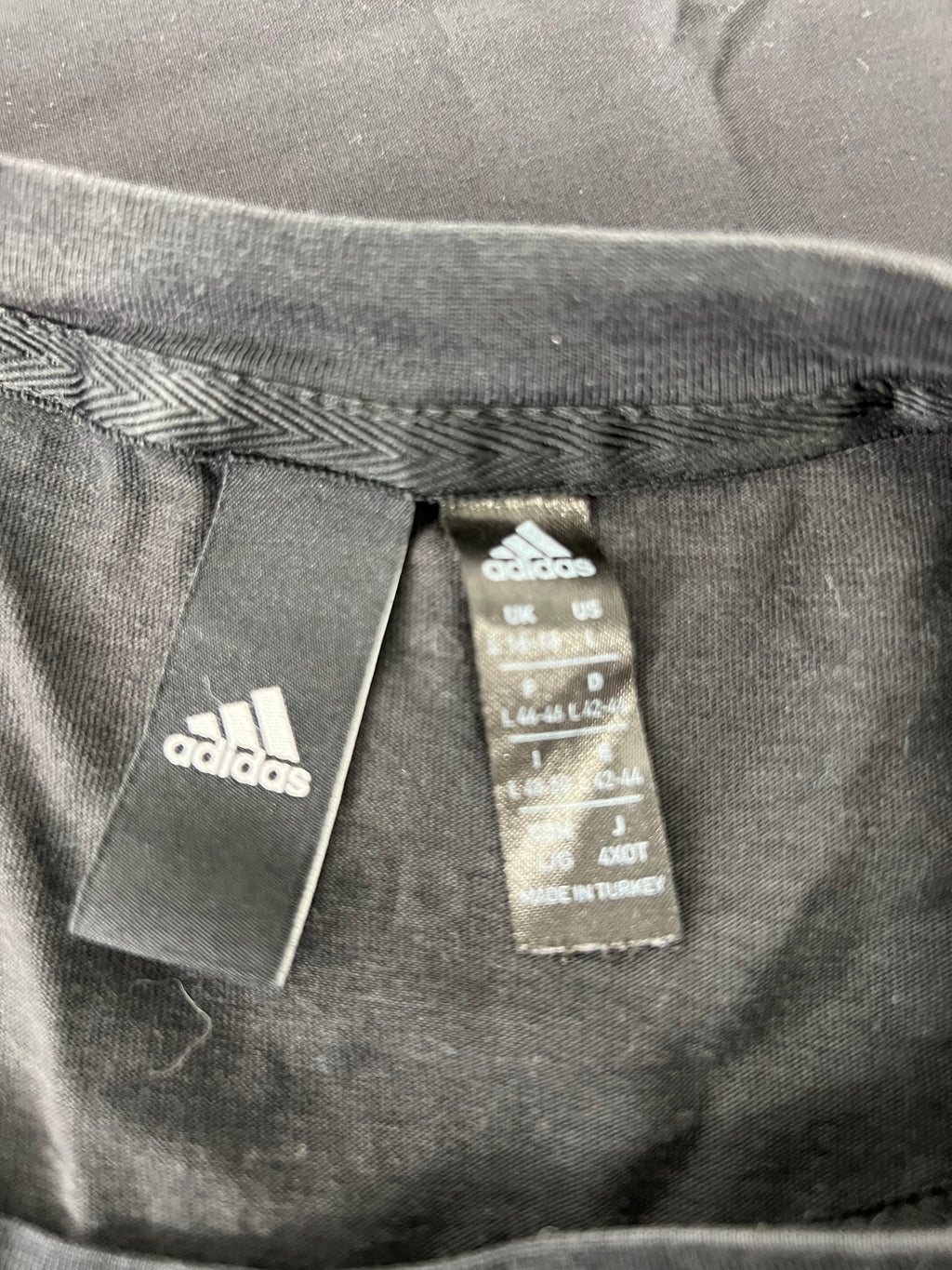 Close-up image of inner tags on Adidas women's black t-shirt showing size and manufacturing details.