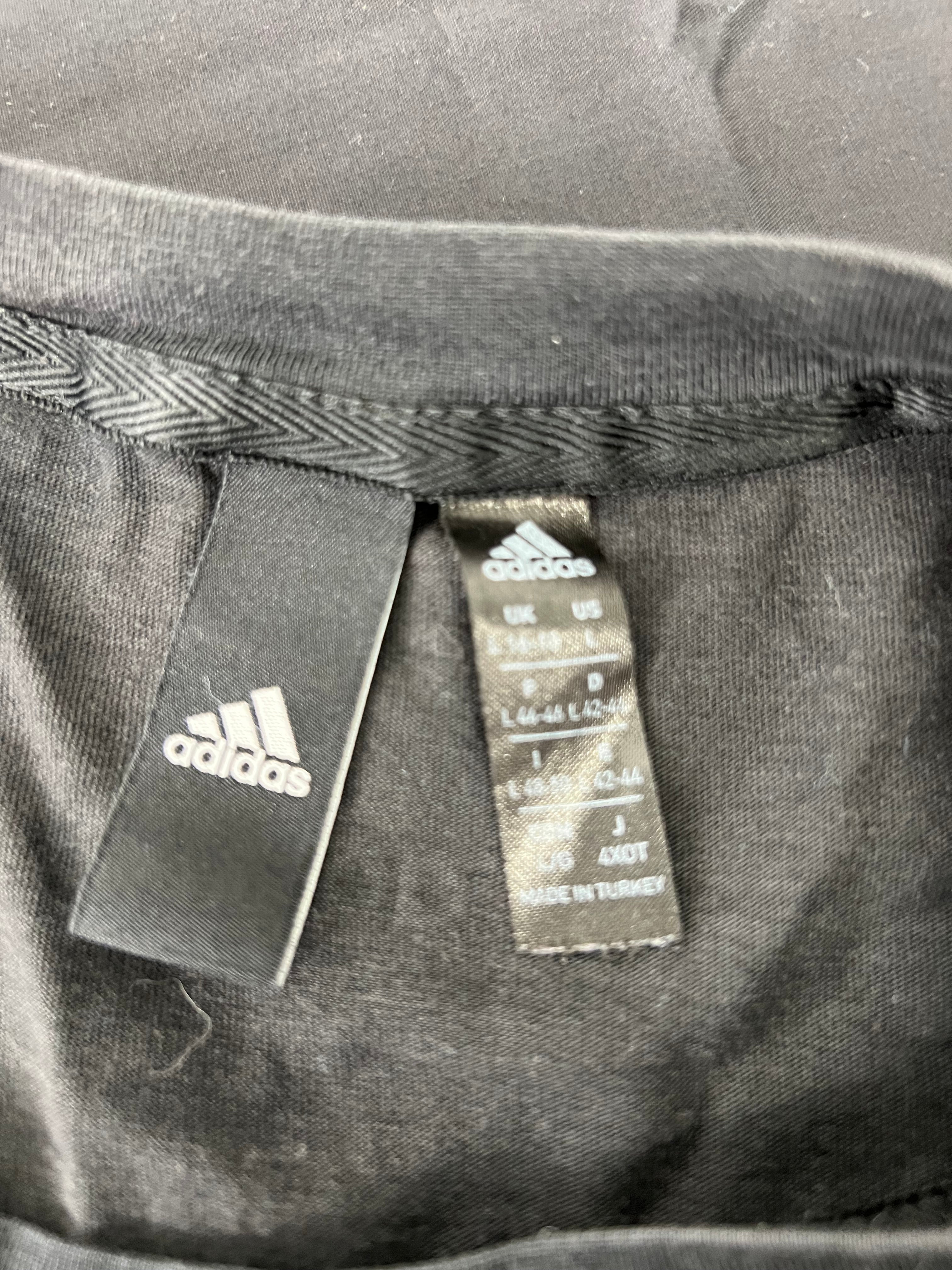 Close-up image of inner tags on Adidas women's black t-shirt showing size and manufacturing details.