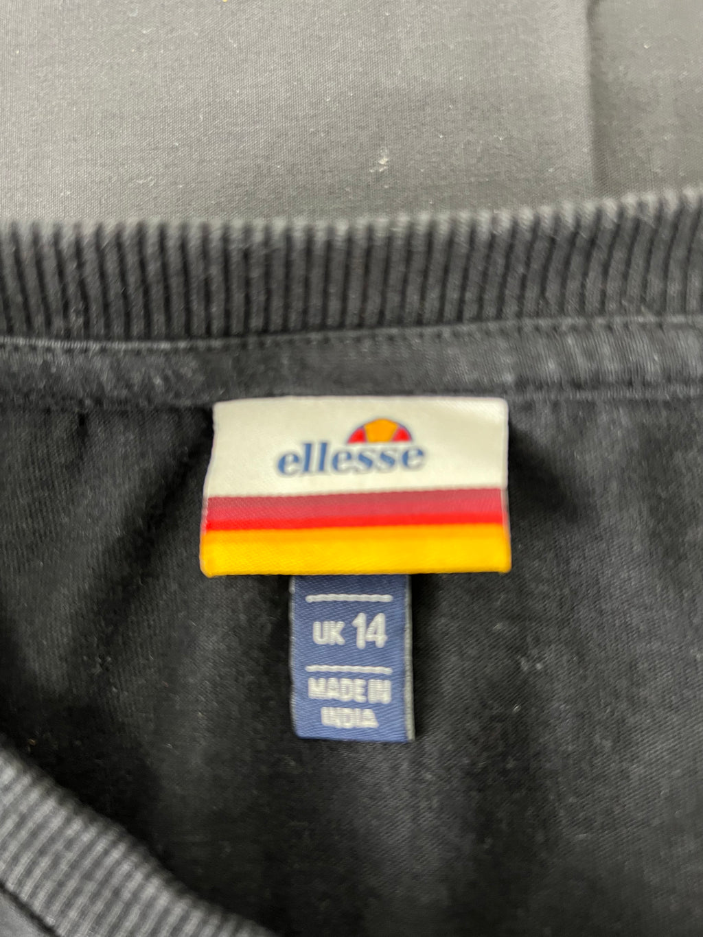 Close-up of ellesse clothing label inside black women's long sleeve top indicating UK size 14 and made in India