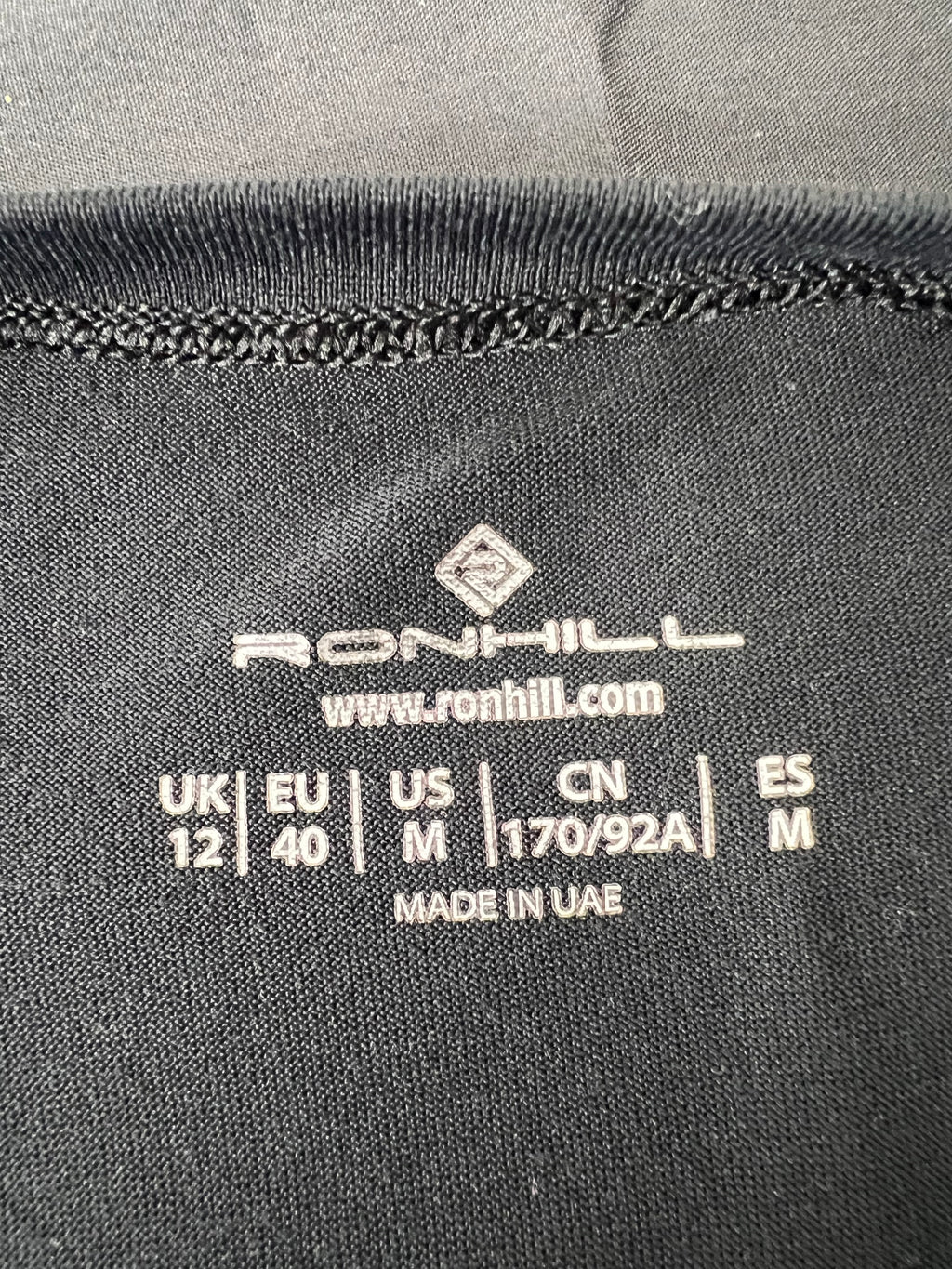 Close-up of Ronhill label inside black t-shirt showing size UK 12 EU 40 US M and manufacturing details