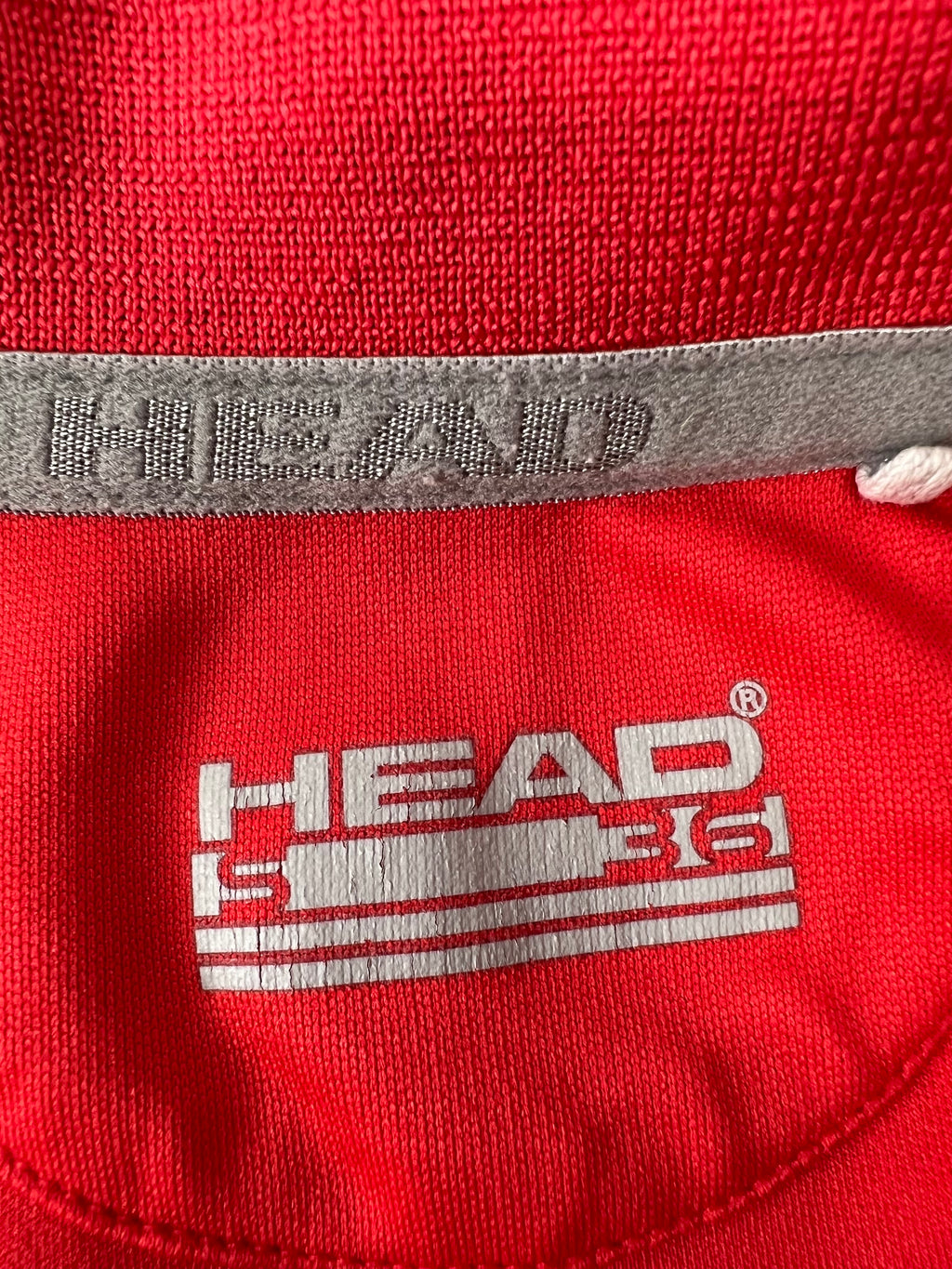 Close-up of inside collar showing HEAD logo print and stitched label on red fabric polo shirt