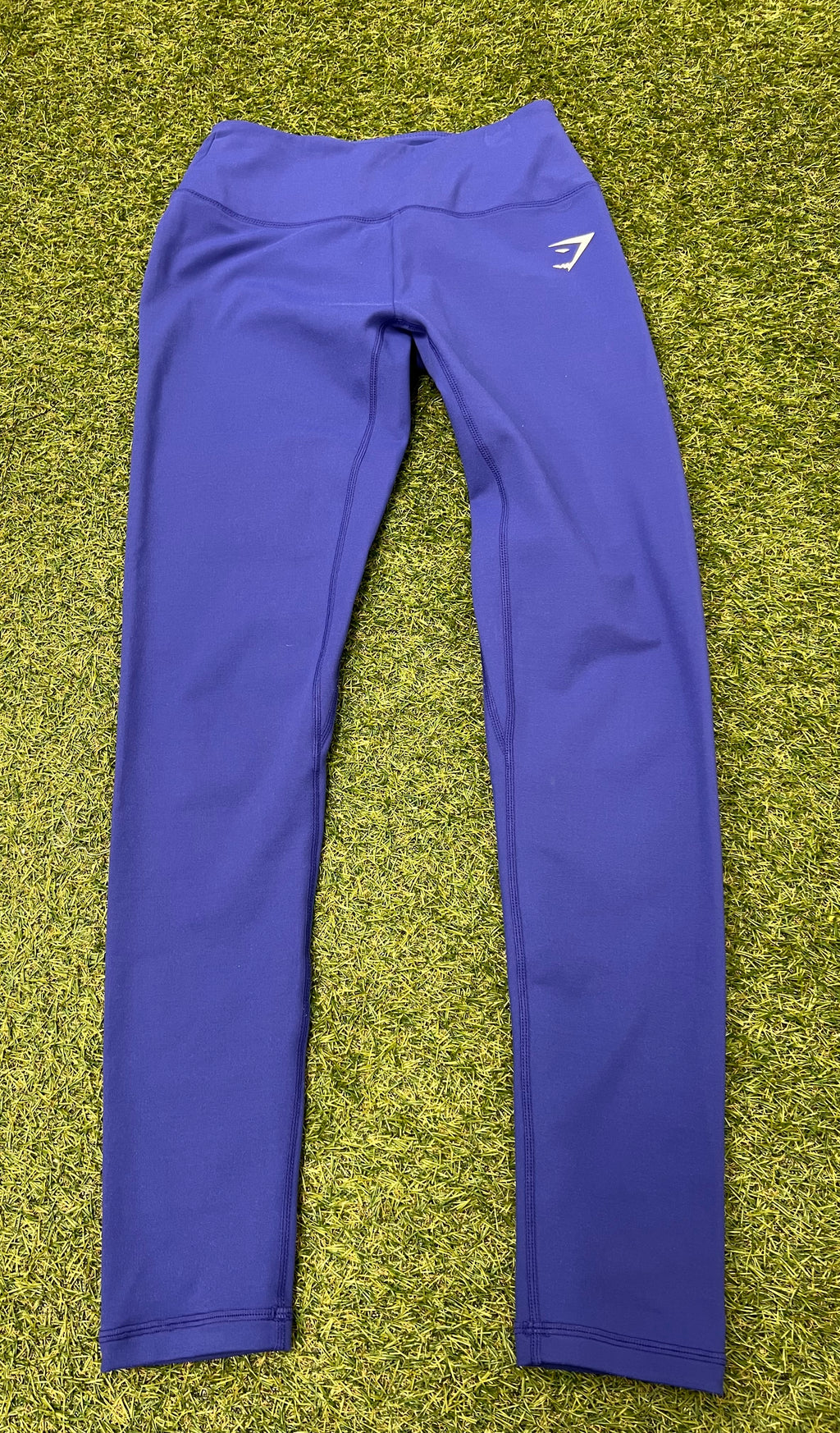 Front view of blue Gymshark moisture management leggings laid flat on grass