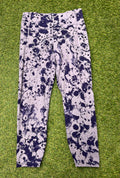 Front view of Under Armour fitted leggings with a black and white splash pattern on lavender background laid on grass