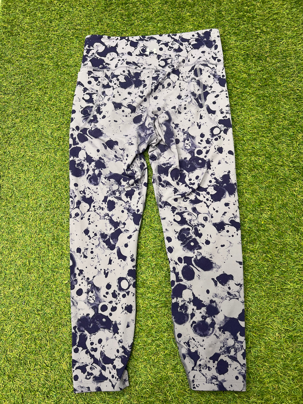 Back view of Under Armour fitted leggings showing the same splash pattern laid flat on grass