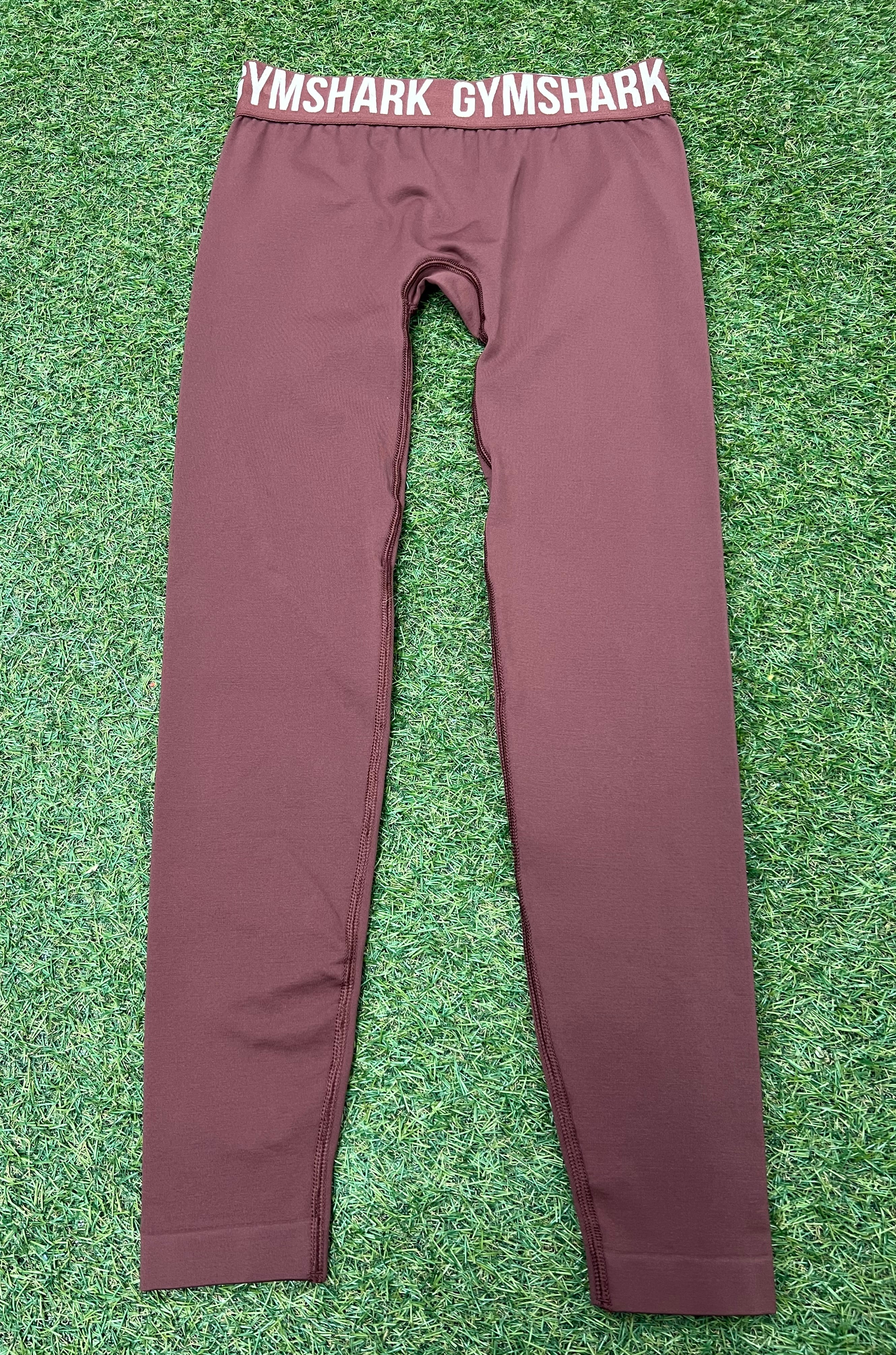 Front view of maroon Gymshark leggings laid flat on grass showing elastic waistband with Gymshark logo
