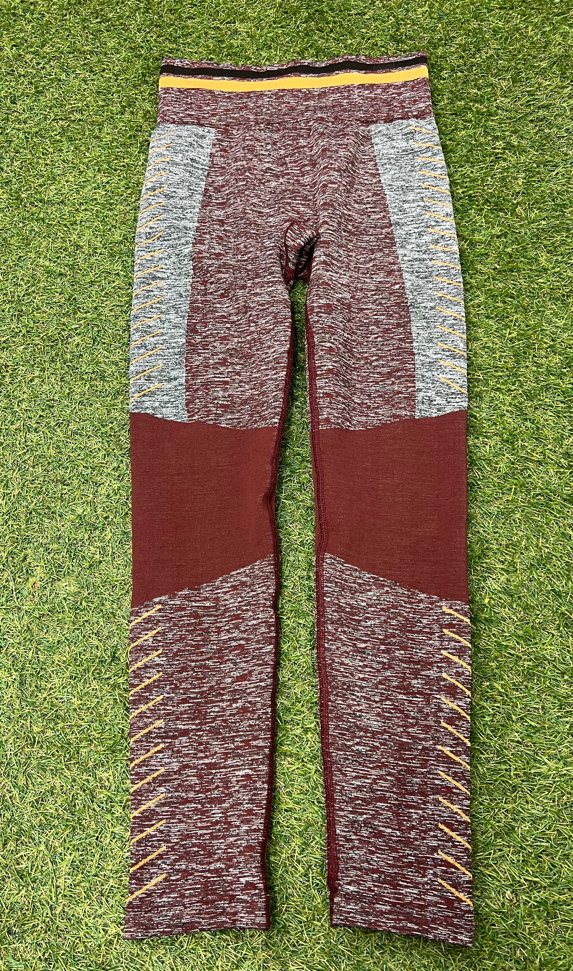 Front view of maroon and grey seamless Sweaty Betty leggings with yellow detailing on grass background