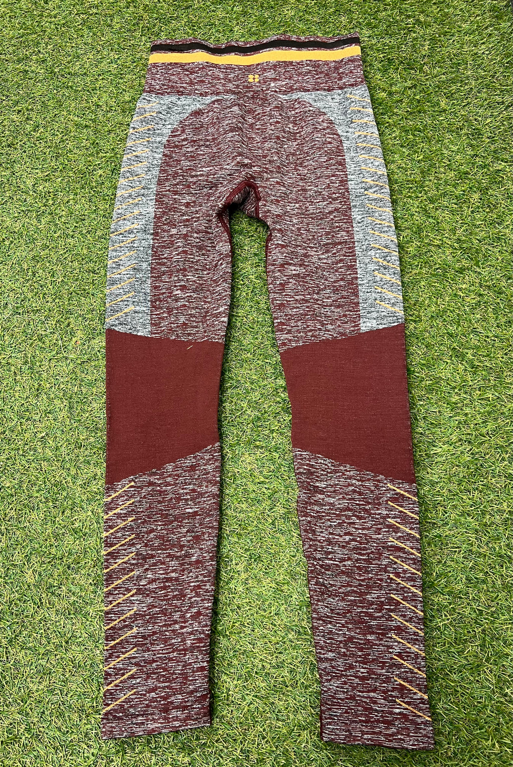 Back view of maroon and grey seamless Sweaty Betty leggings with yellow detailing on grass background