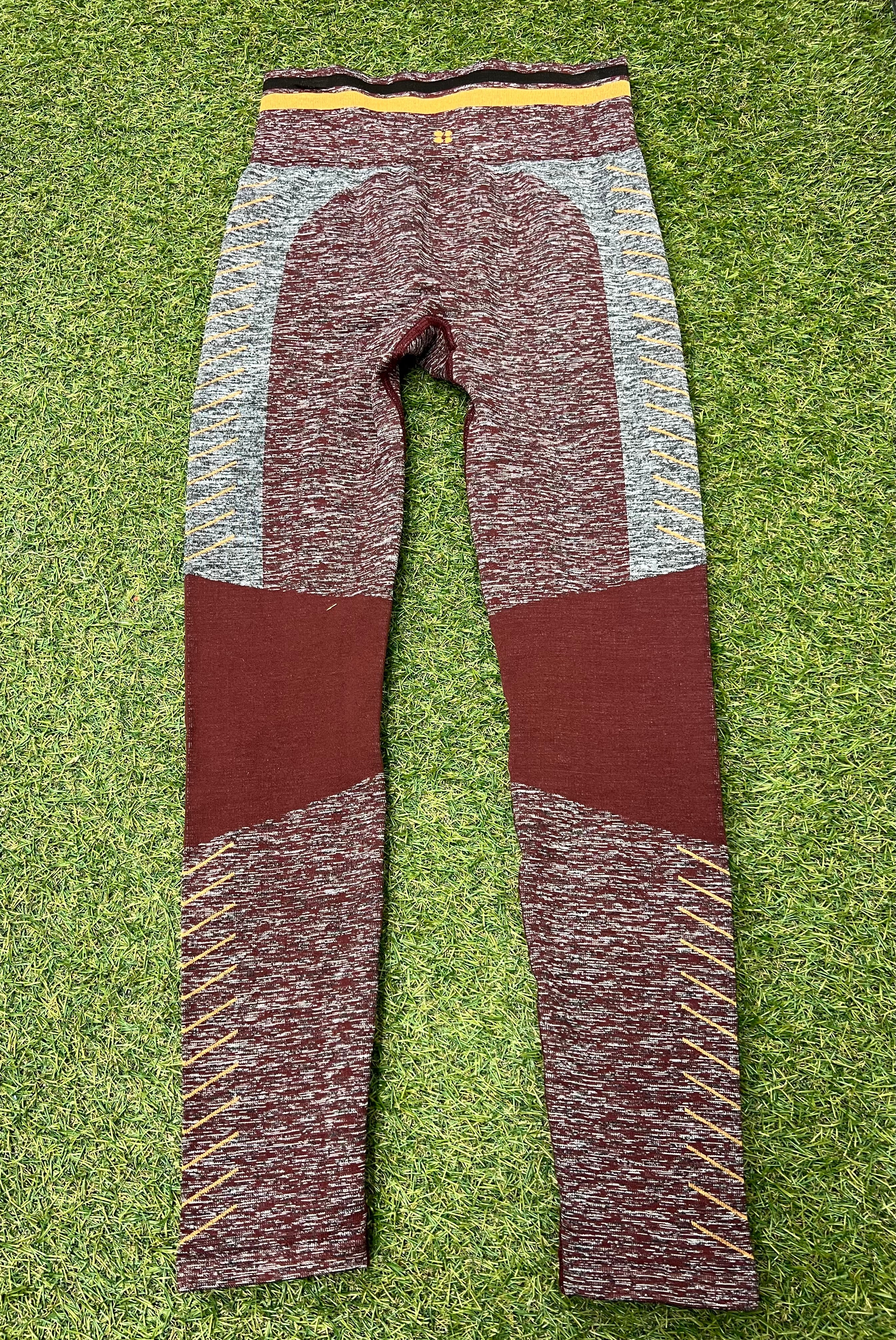 Back view of maroon and grey seamless Sweaty Betty leggings with yellow detailing on grass background