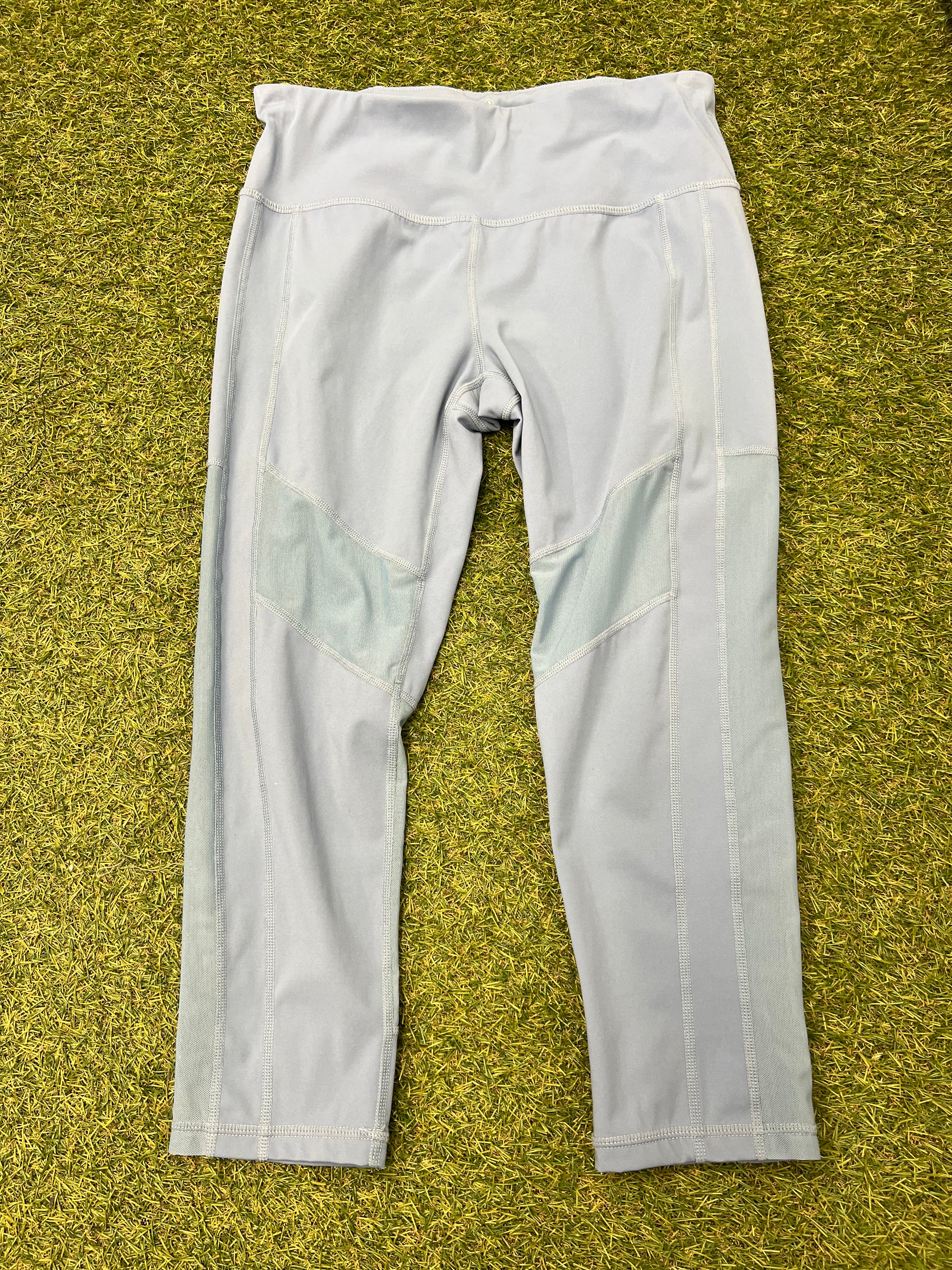 Front view of pale grey Sweaty Betty leggings with mesh inserts laid on grass