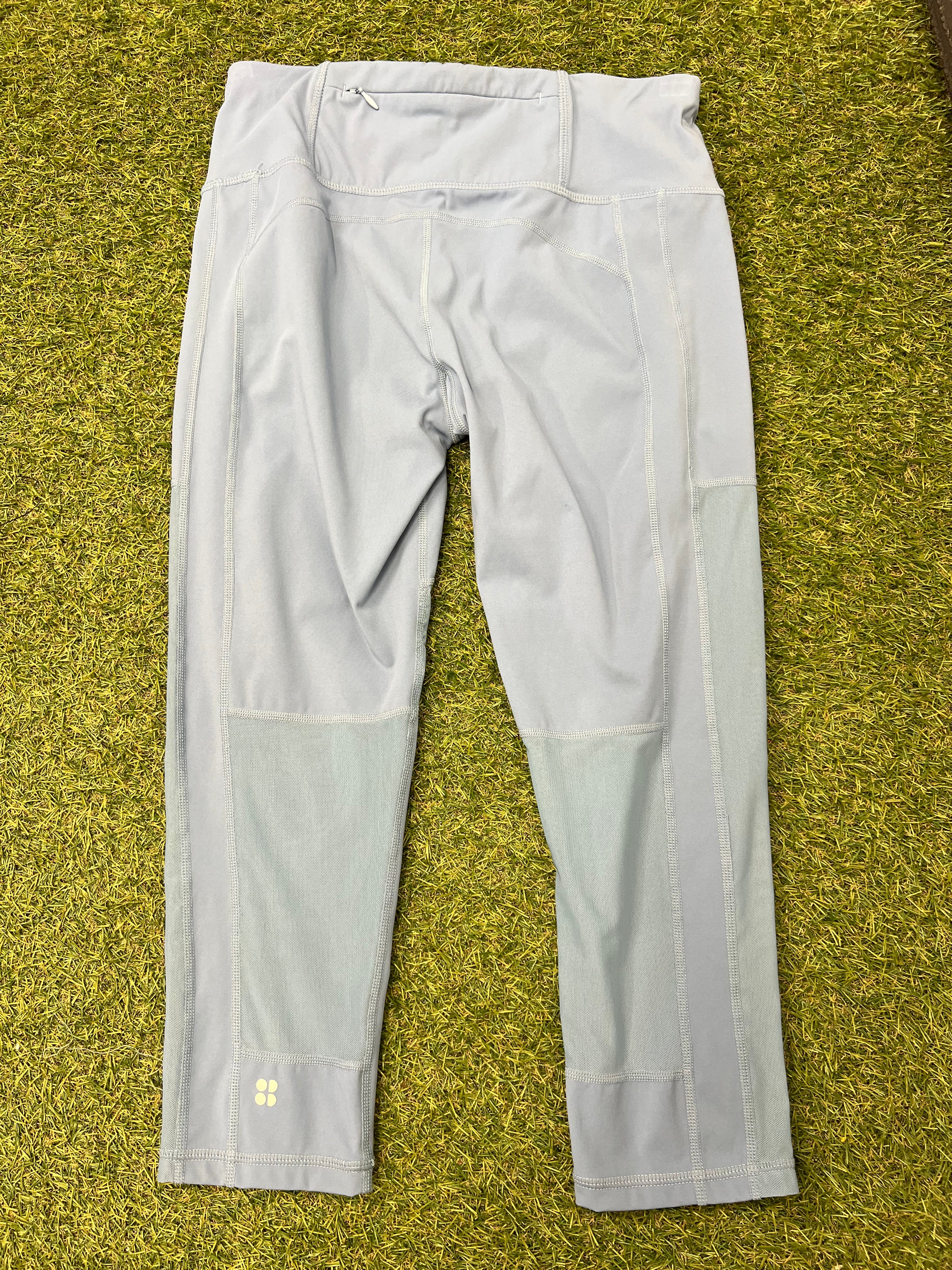 Back view of pale grey Sweaty Betty leggings showing back pocket and mesh panels laid on grass