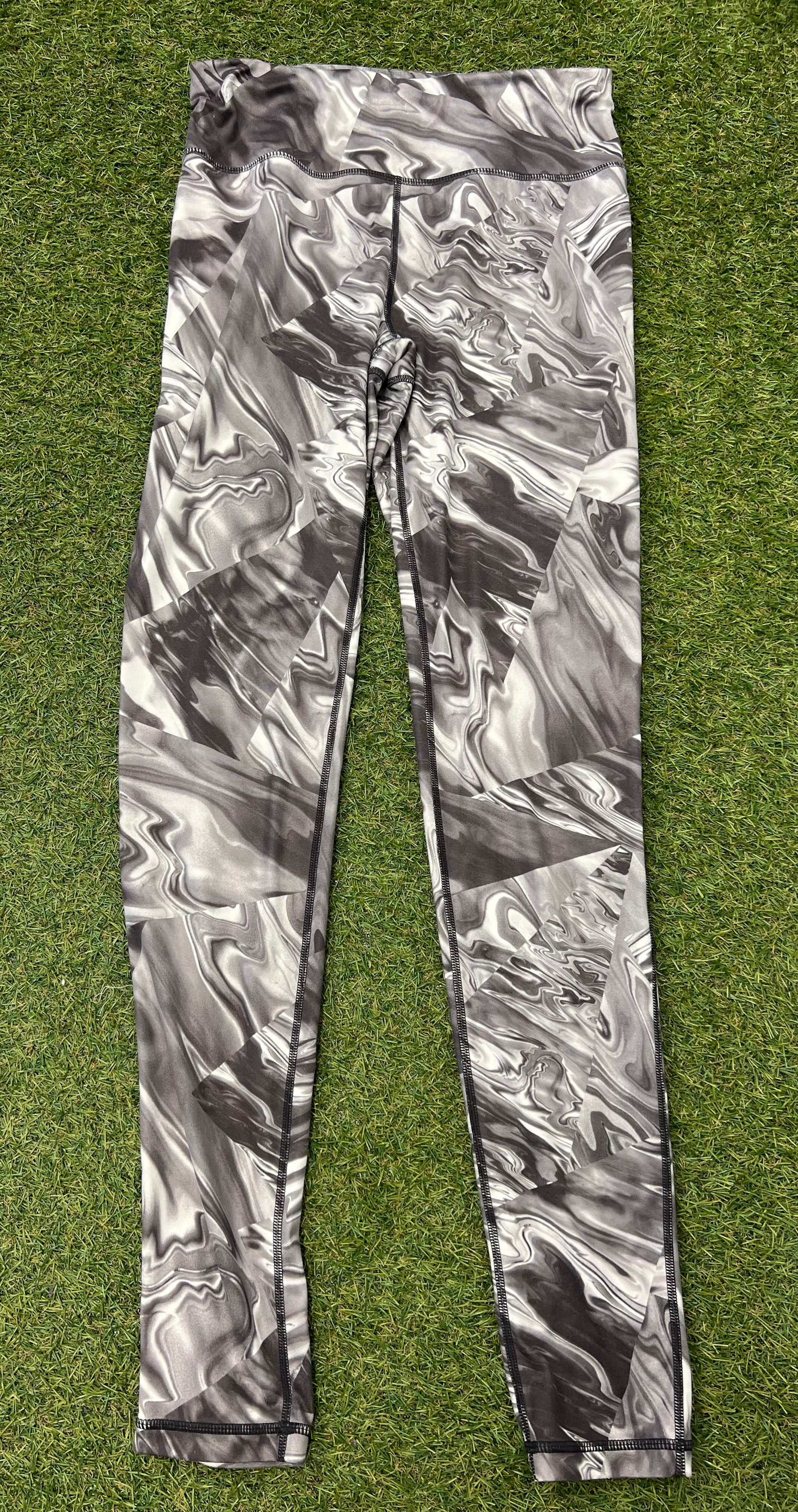 Front view of Sweaty Betty leggings with abstract grey and black marbled print laid flat on grass