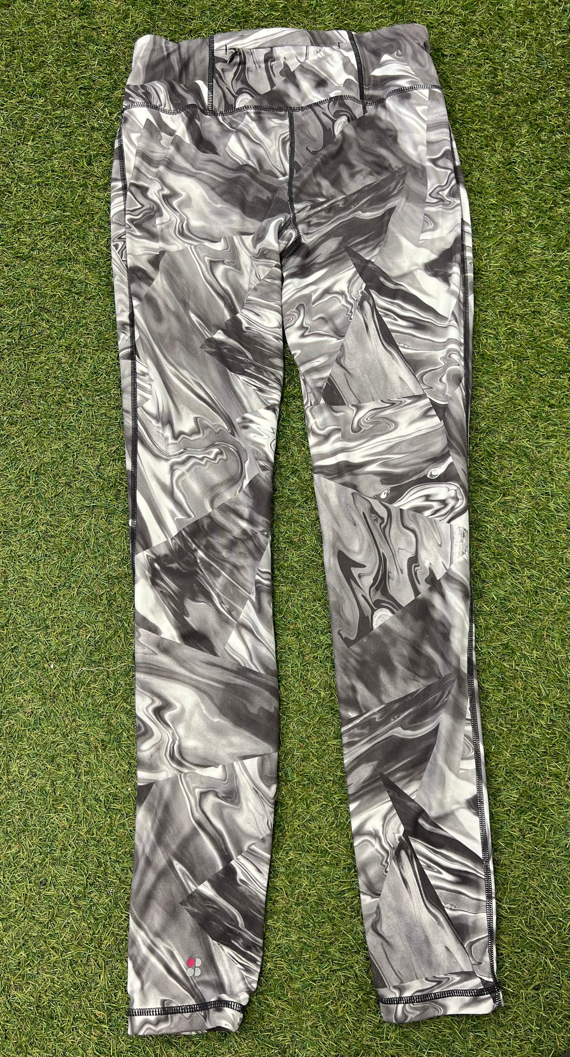 Back view of Sweaty Betty leggings showing high waistband and marbled print laid flat on grass