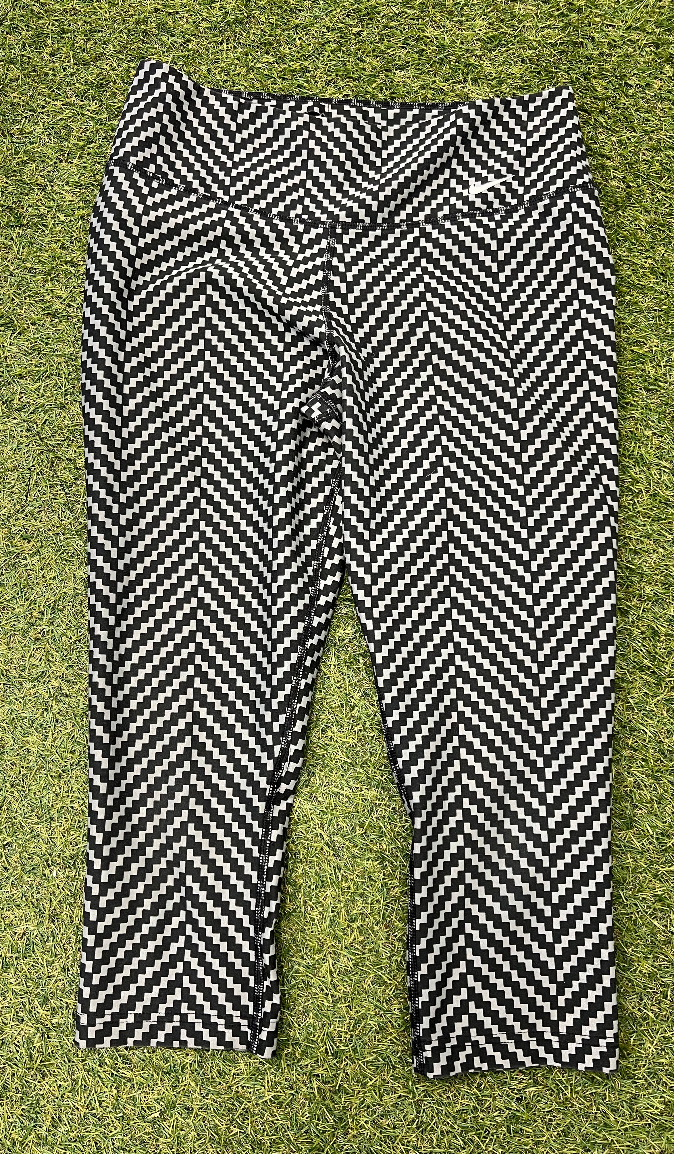 Front view of Nike Dri-FIT black and white zigzag patterned crop leggings laid flat on grass