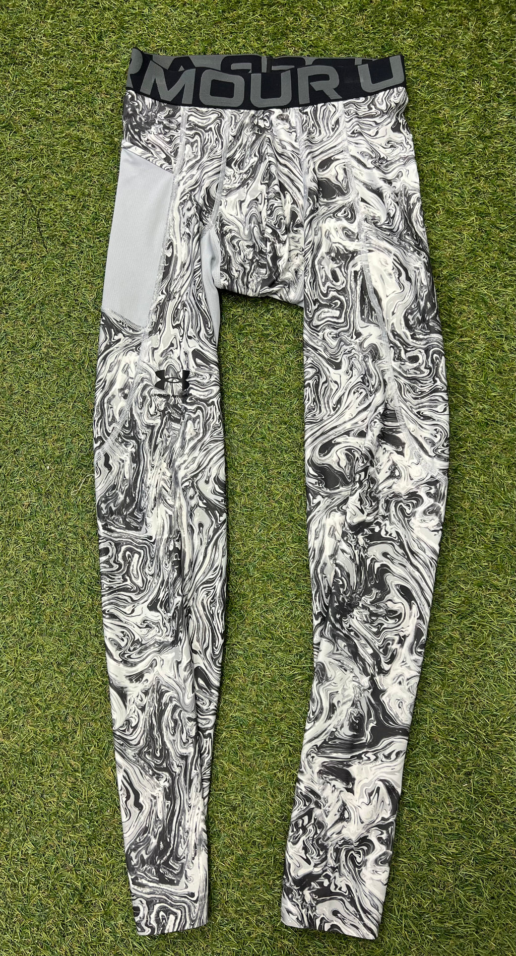 Front view of Under Armour mens compression tights featuring black and white marbled pattern and black elastic waistband with logo on grass background