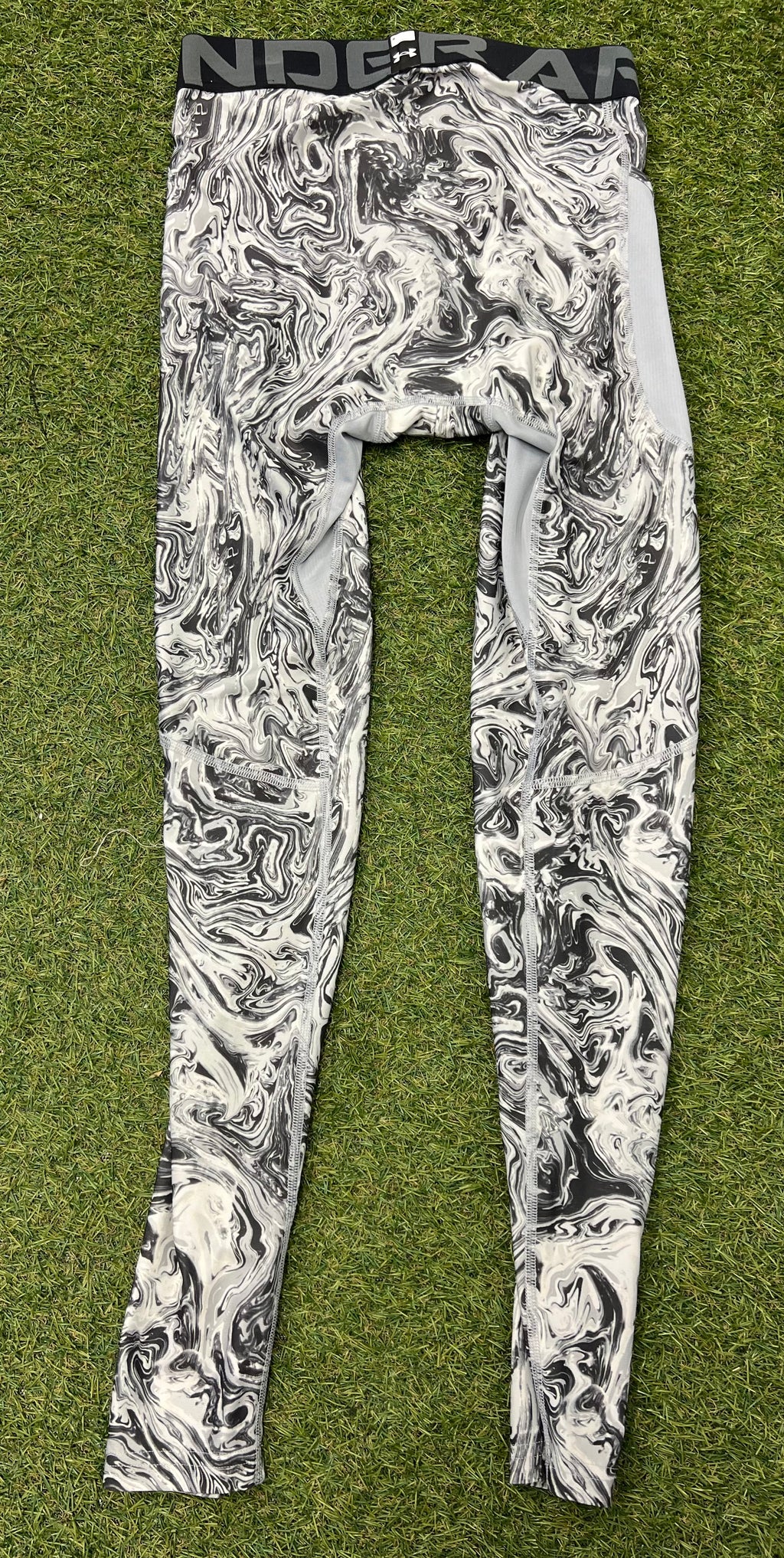 Back view of Under Armour mens compression tights highlighting marbled pattern and mesh ventilation panels on grass background