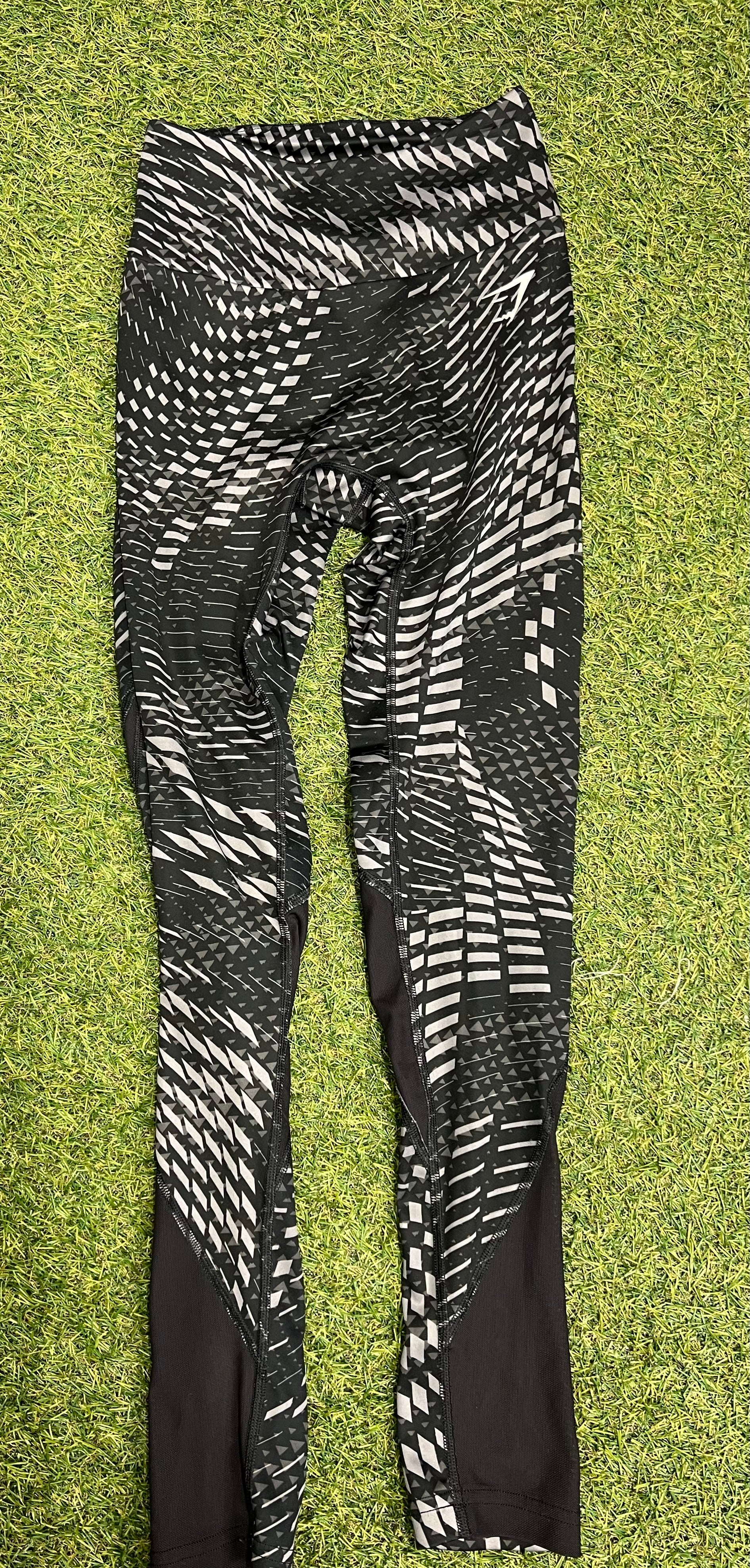Front view of Gymshark black and white geometric print performance leggings laid flat on grass