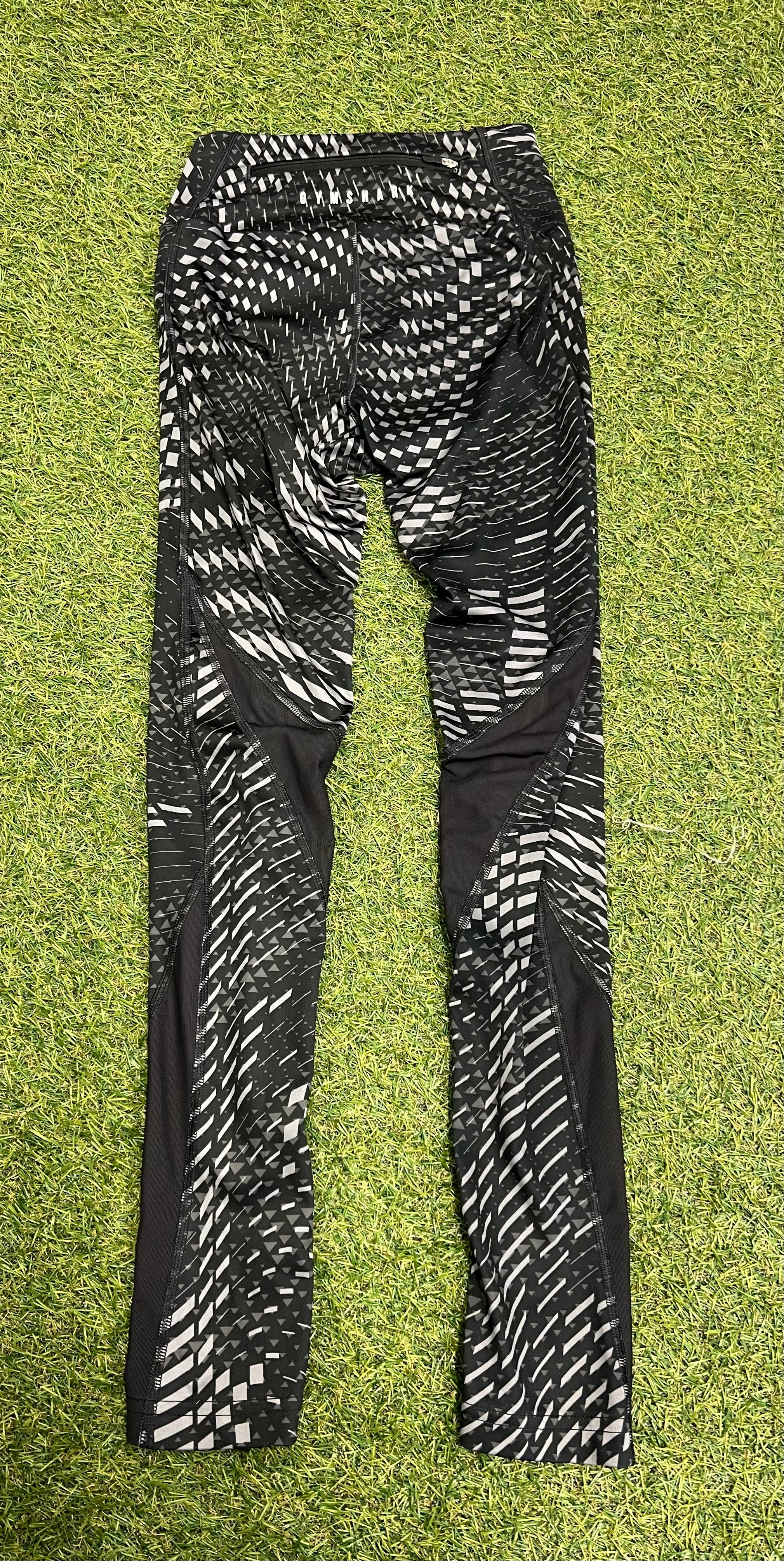 Back view of Gymshark black and white geometric print leggings with mesh panels on lower legs, laid flat on grass