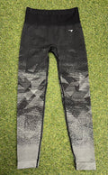 Front view of black and grey ombre Gymshark leggings with geometric pattern laid flat on grass