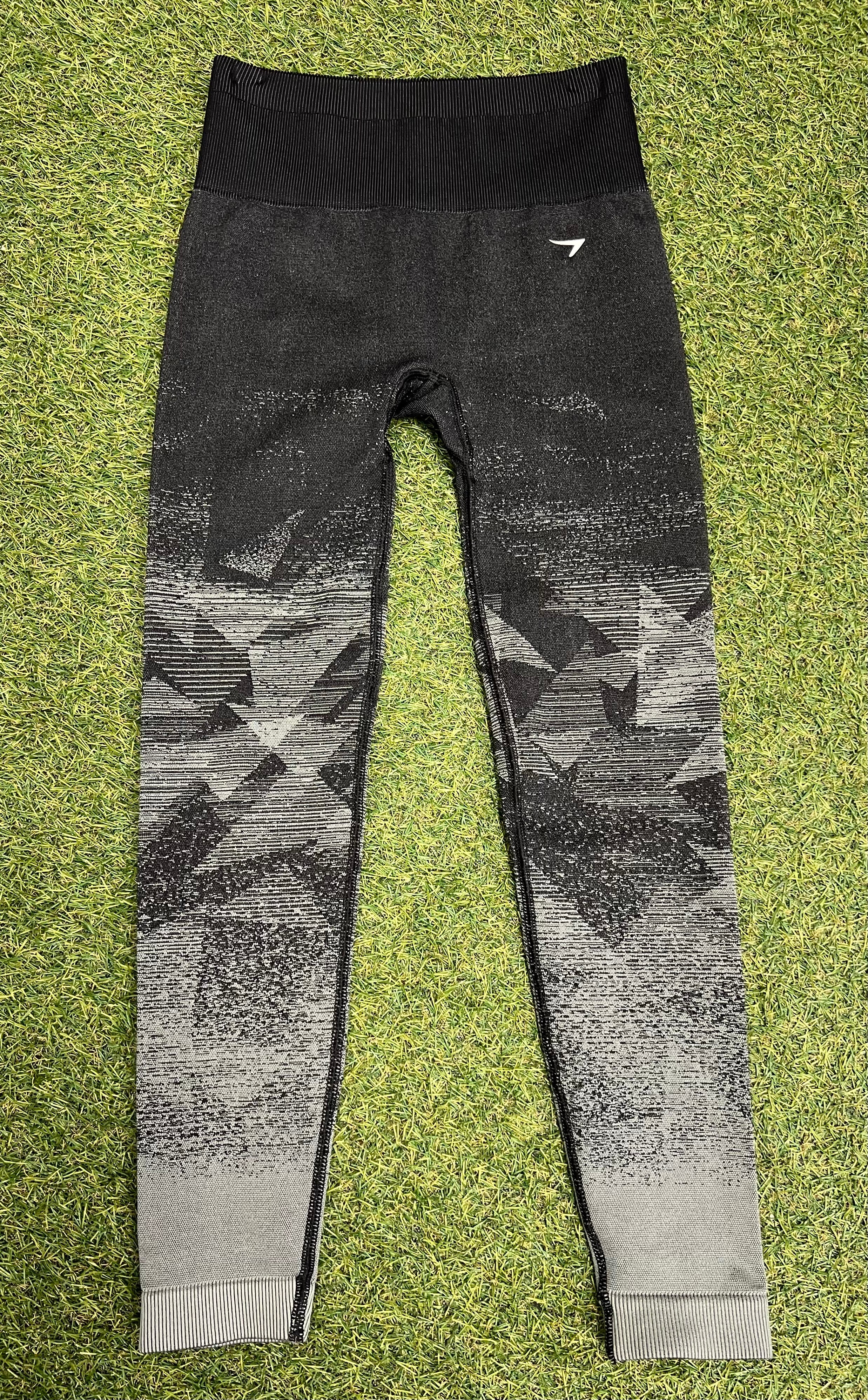 Front view of black and grey ombre Gymshark leggings with geometric pattern laid flat on grass