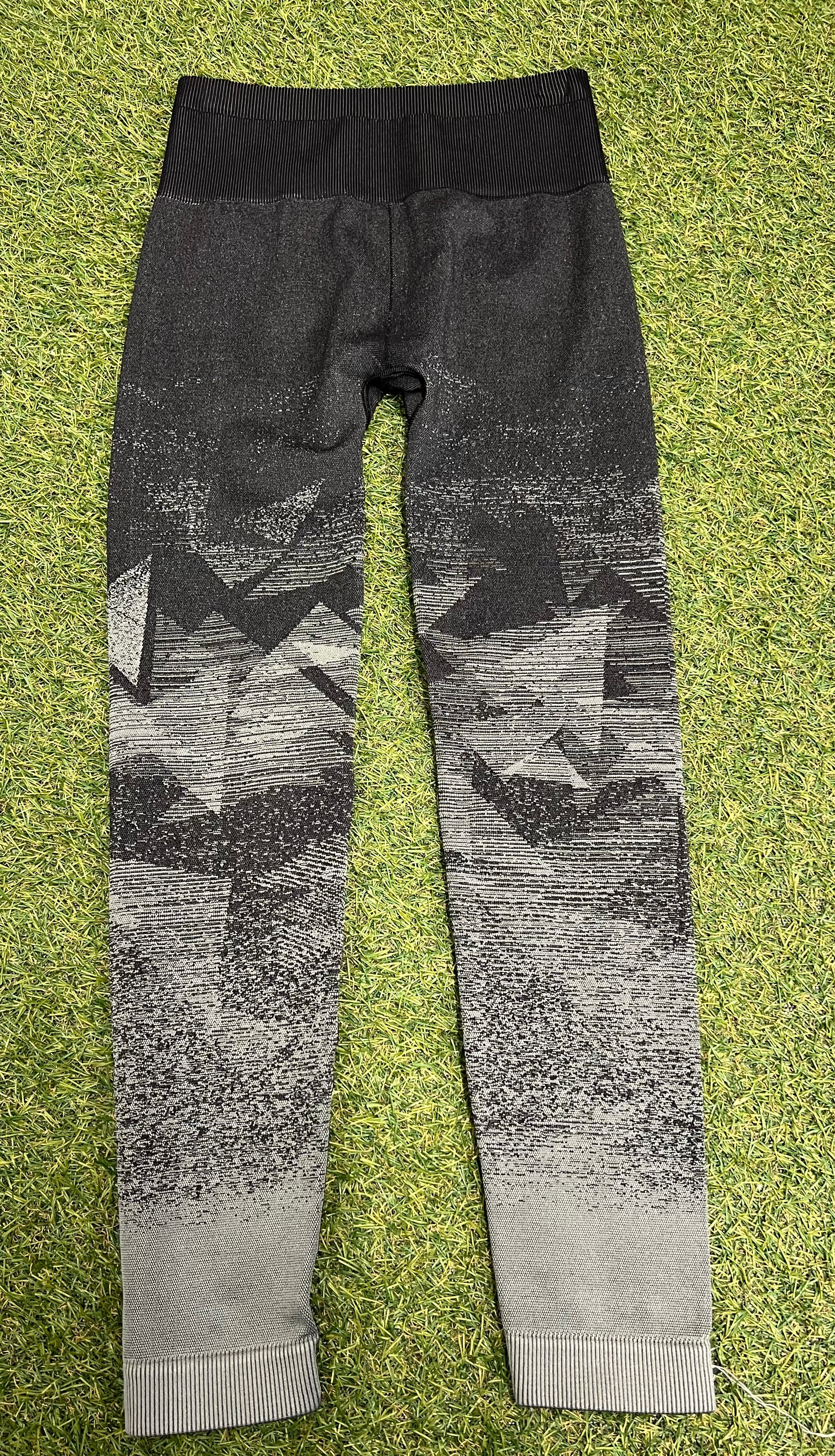 Back view of black and grey ombre Gymshark leggings showing seamless design and geometric pattern laid flat on grass