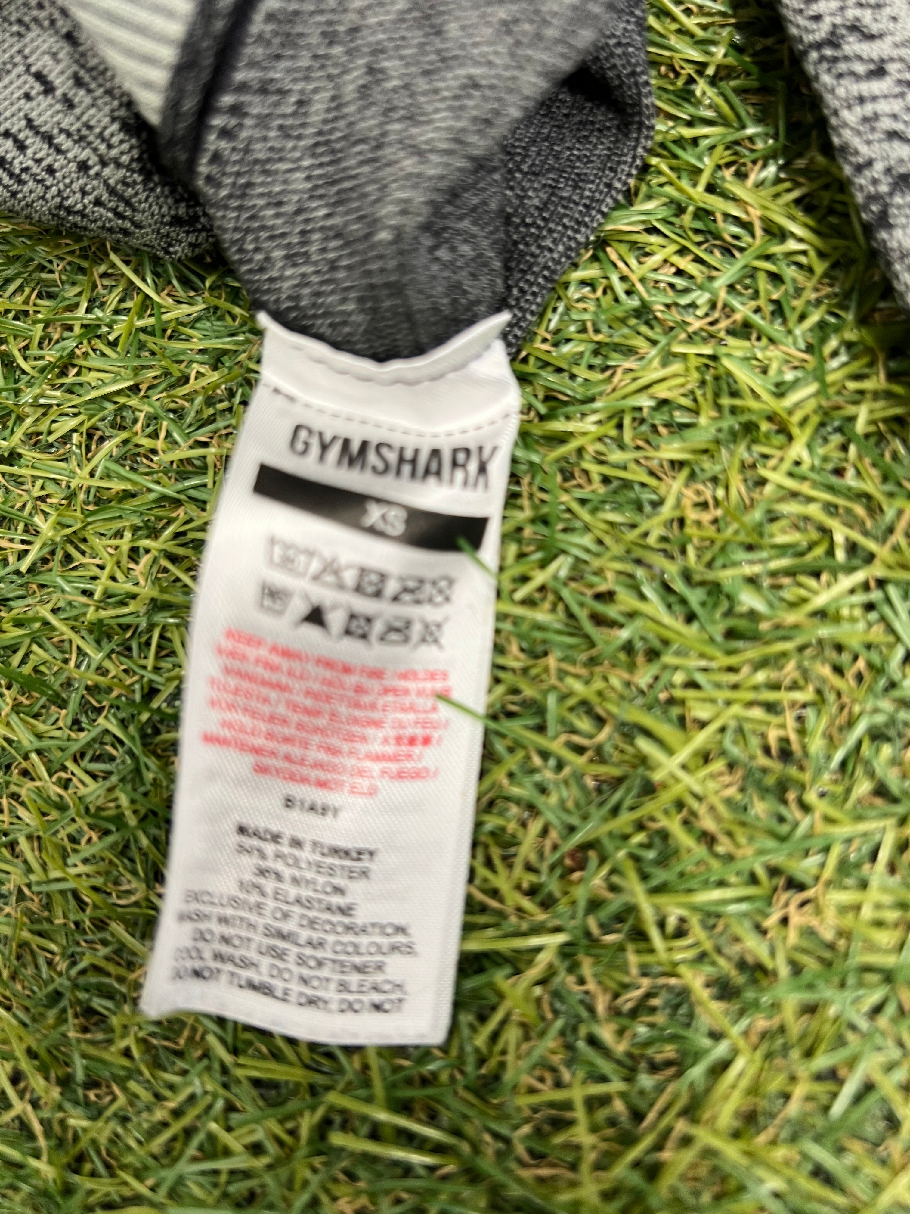 Close-up of Gymshark clothing tag showing care instructions and fabric composition on grass background