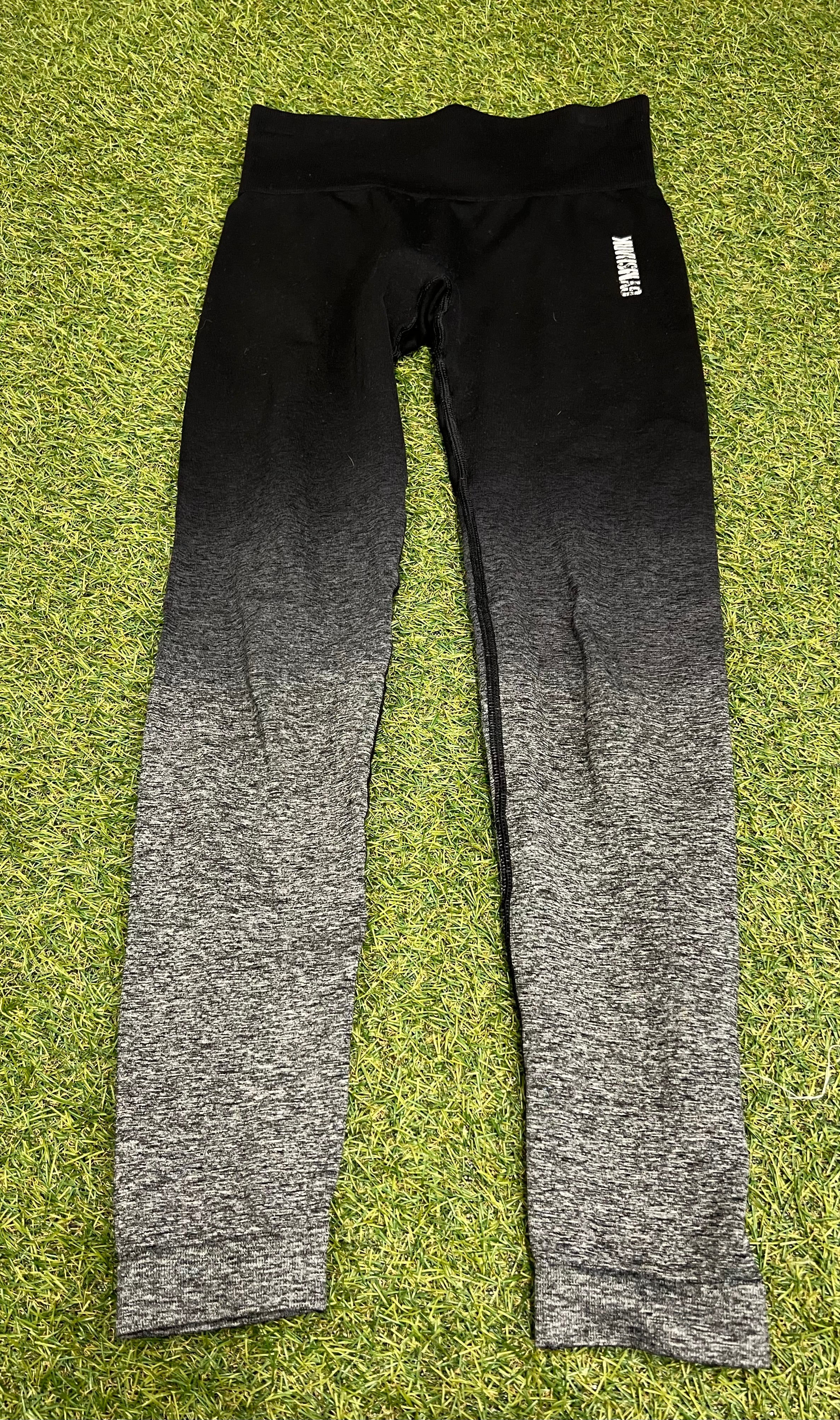 Front view of Gymshark Ombre Seamless Leggings lying flat on grass, showing black to grey gradient and Gymshark branding on hip