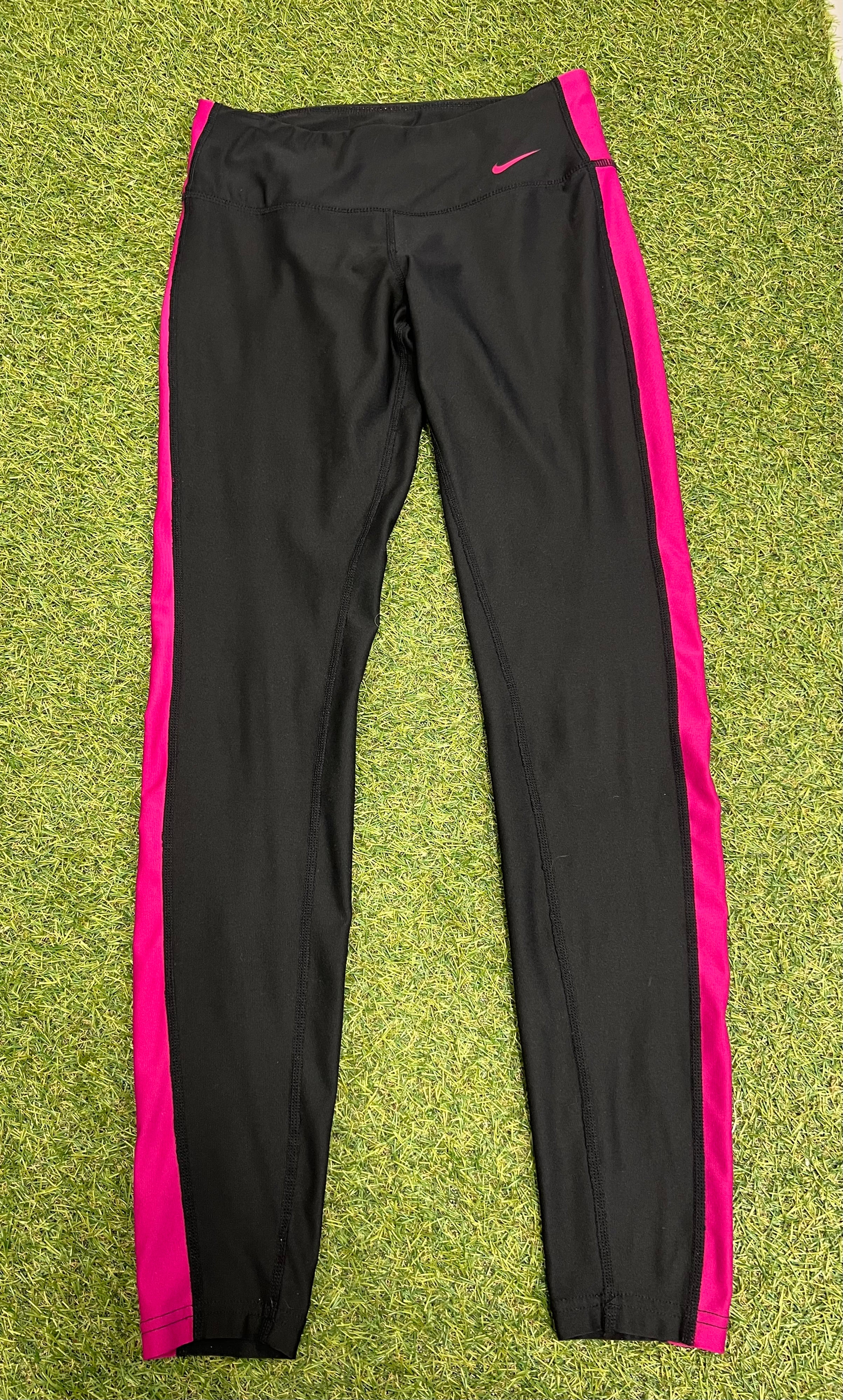 Front view of Nike Dri-FIT black leggings with pink side panels laid flat on grass