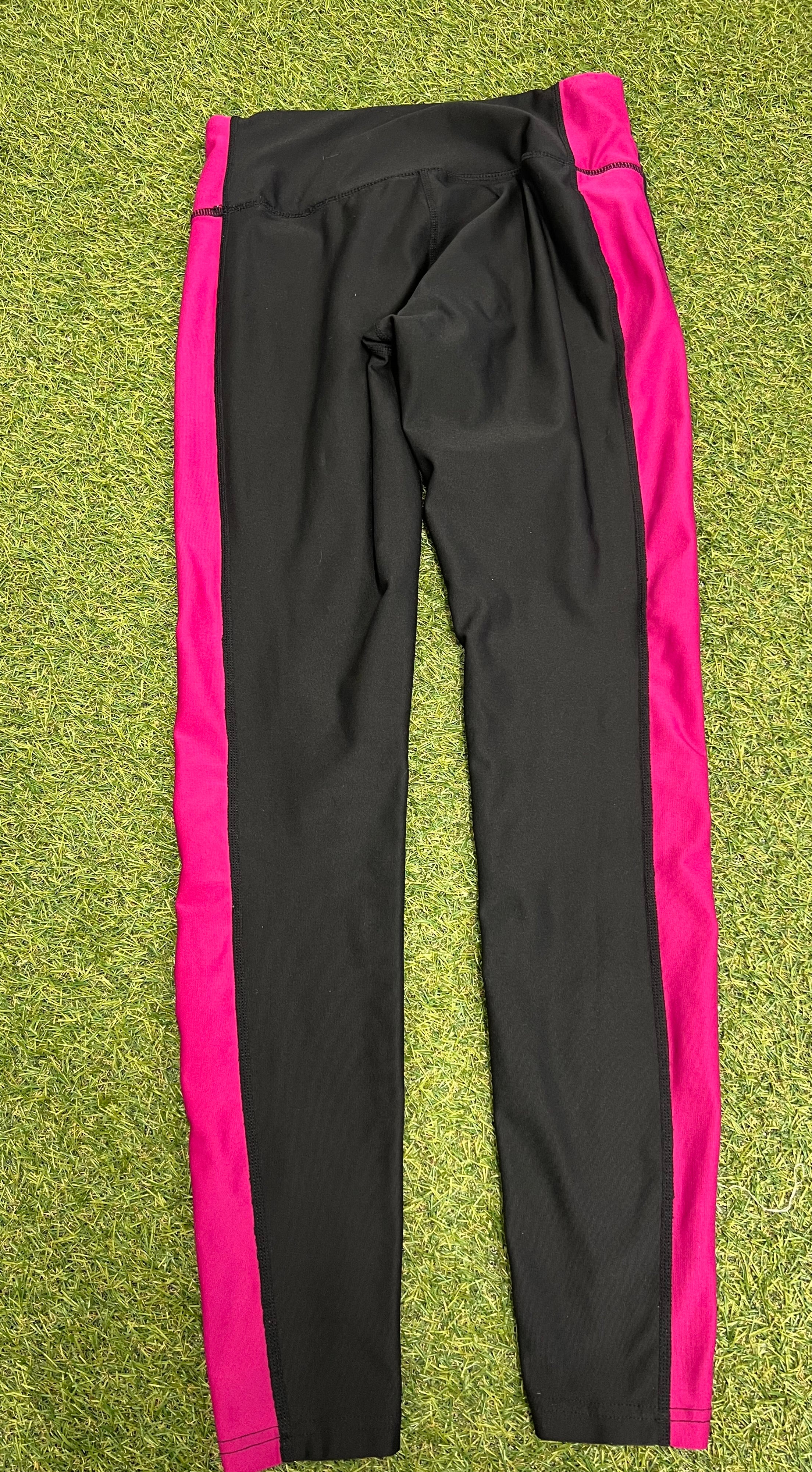 Rear view of Nike Dri-FIT black leggings with pink side panels laid flat on grass