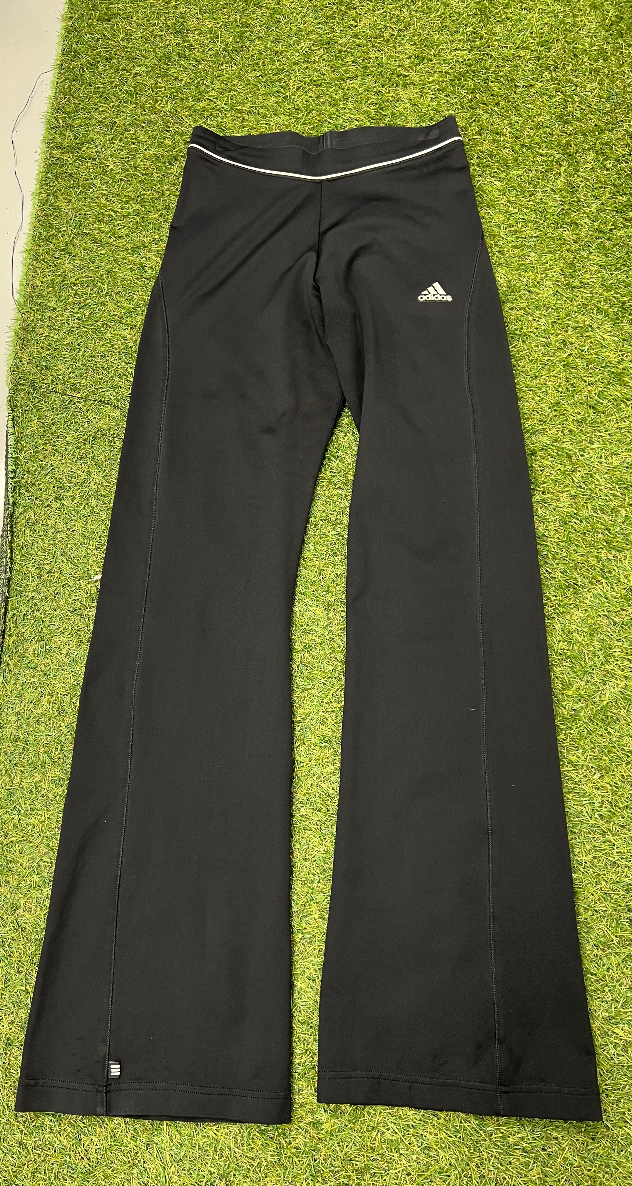Front view of Adidas black yoga pants with reflective waistband detail on green turf
