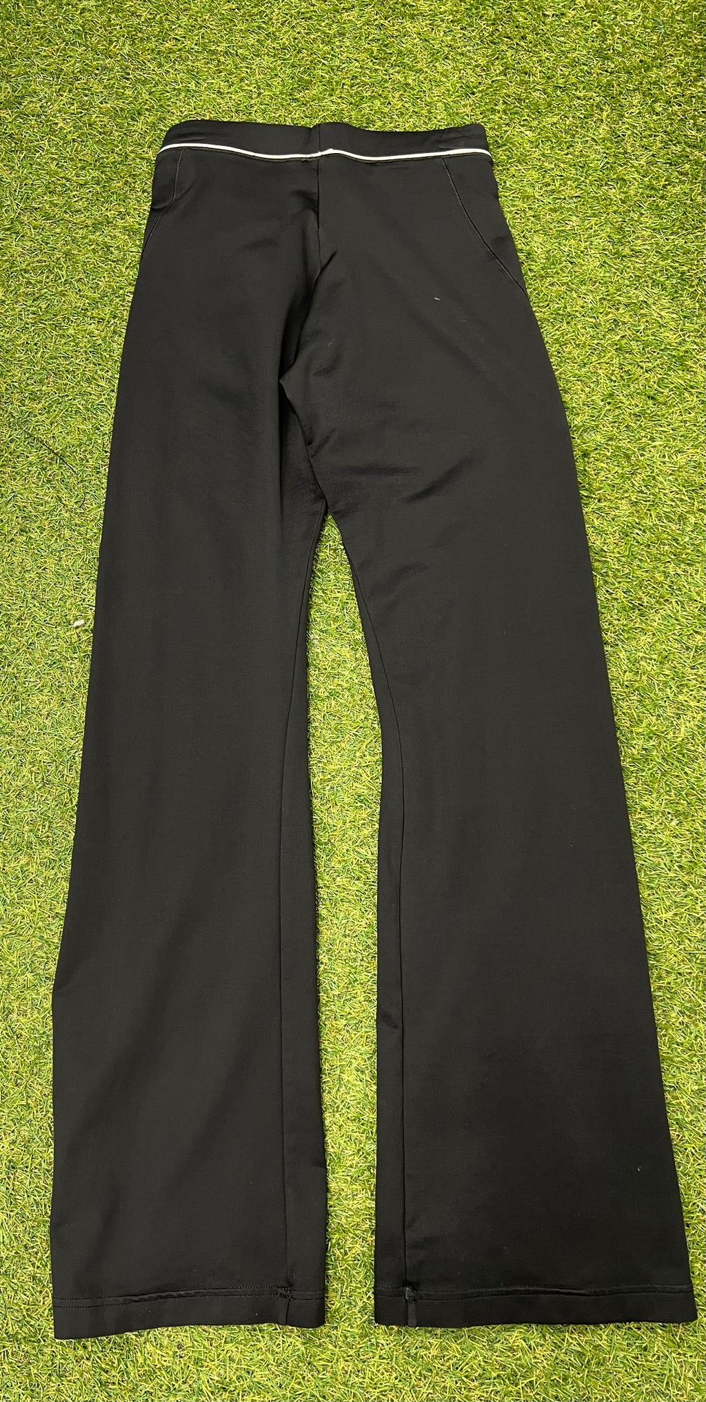 Back view of Adidas black yoga pants showing plain design and waistband detail on green turf