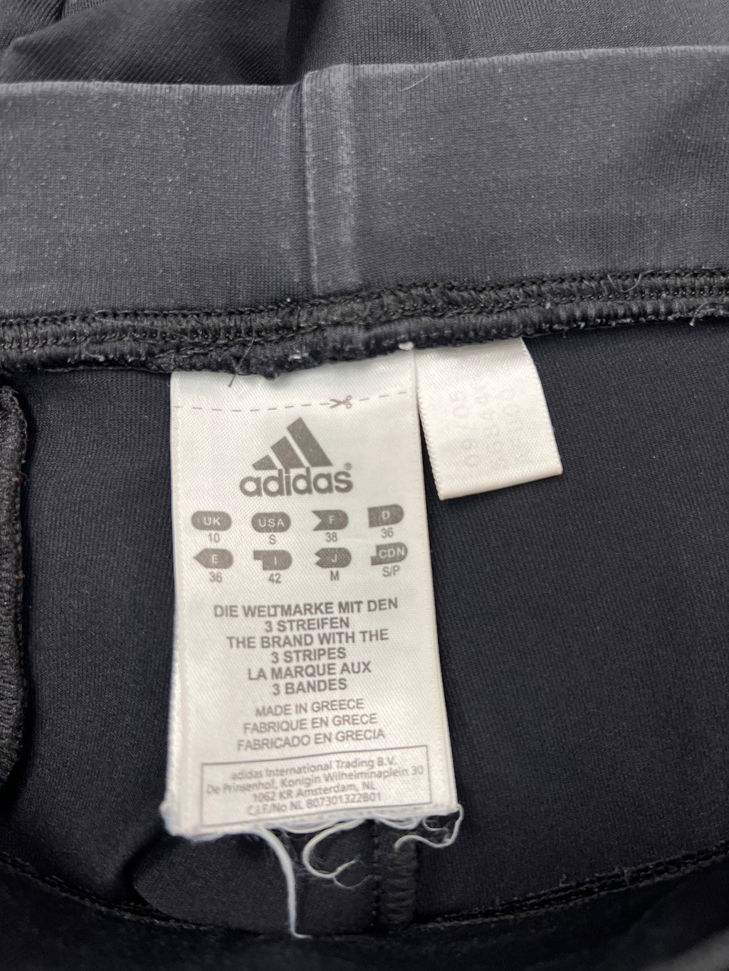 Close-up of Adidas brand tag inside black yoga pants showing sizing and manufacturing info