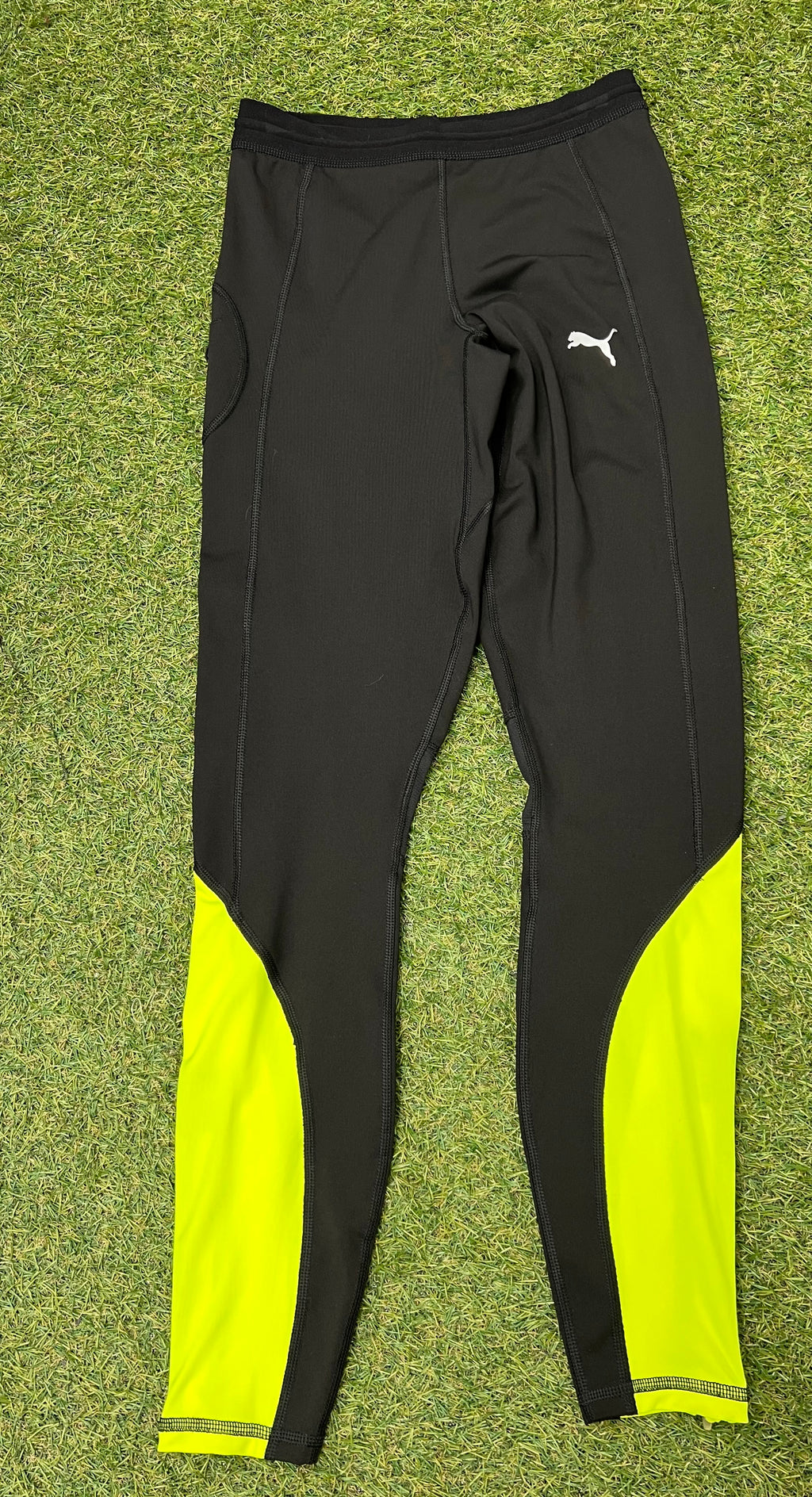 Front view of black Puma leggings with neon yellow panels on calves laid flat on grass