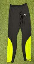 Front view of black Puma leggings with neon yellow panels on calves laid flat on grass