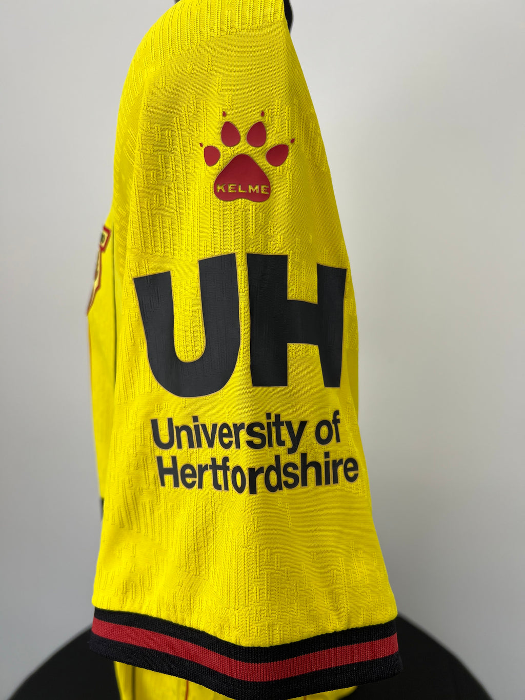 Close-up of right sleeve featuring Kelme paw print logo and University of Hertfordshire sponsor in black on yellow fabric