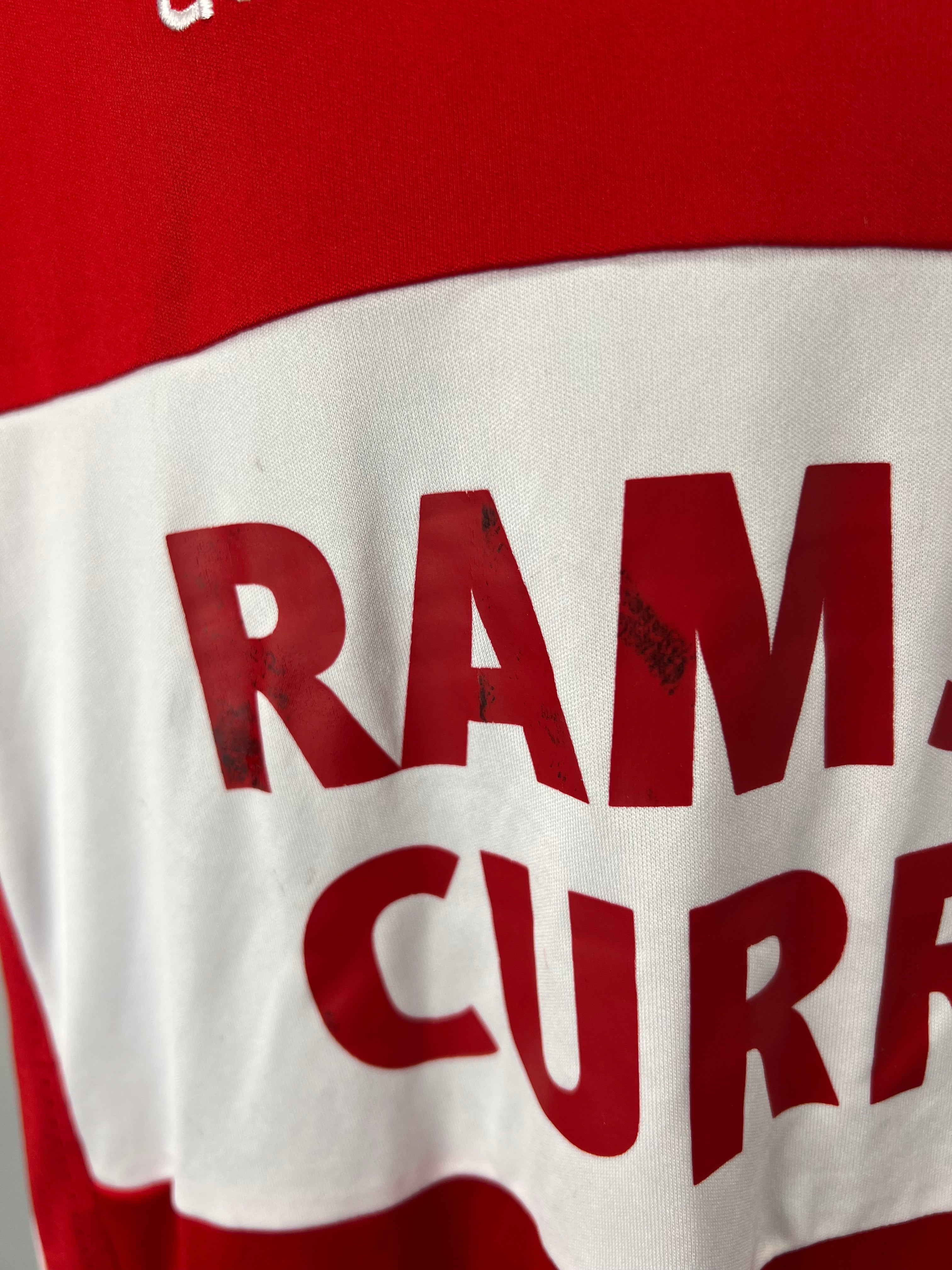 Close-up of Ramsdens Currency sponsor print with some wear marks on the white band of the football shirt