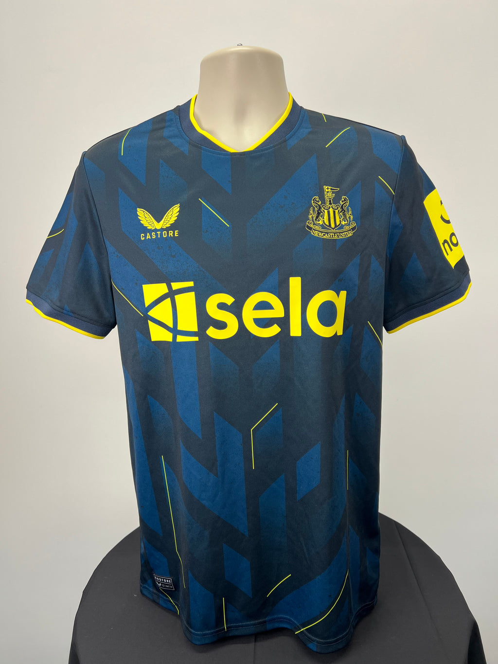 Front view of Newcastle United football shirt in navy and black with yellow sponsor logo and geometric pattern