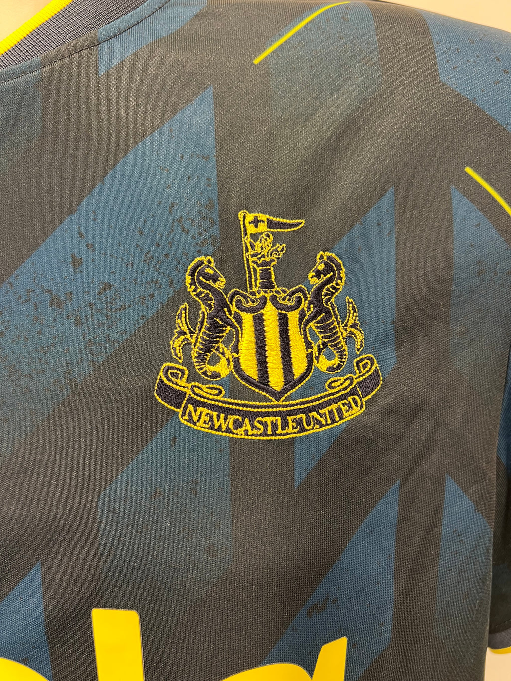 Close-up of embroidered Newcastle United club crest on navy and black football shirt