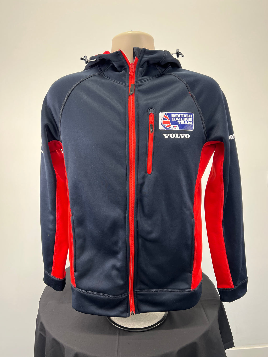 Front view of navy blue Musto British Sailing Team softshell jacket with red side panels and chest zipper pocket